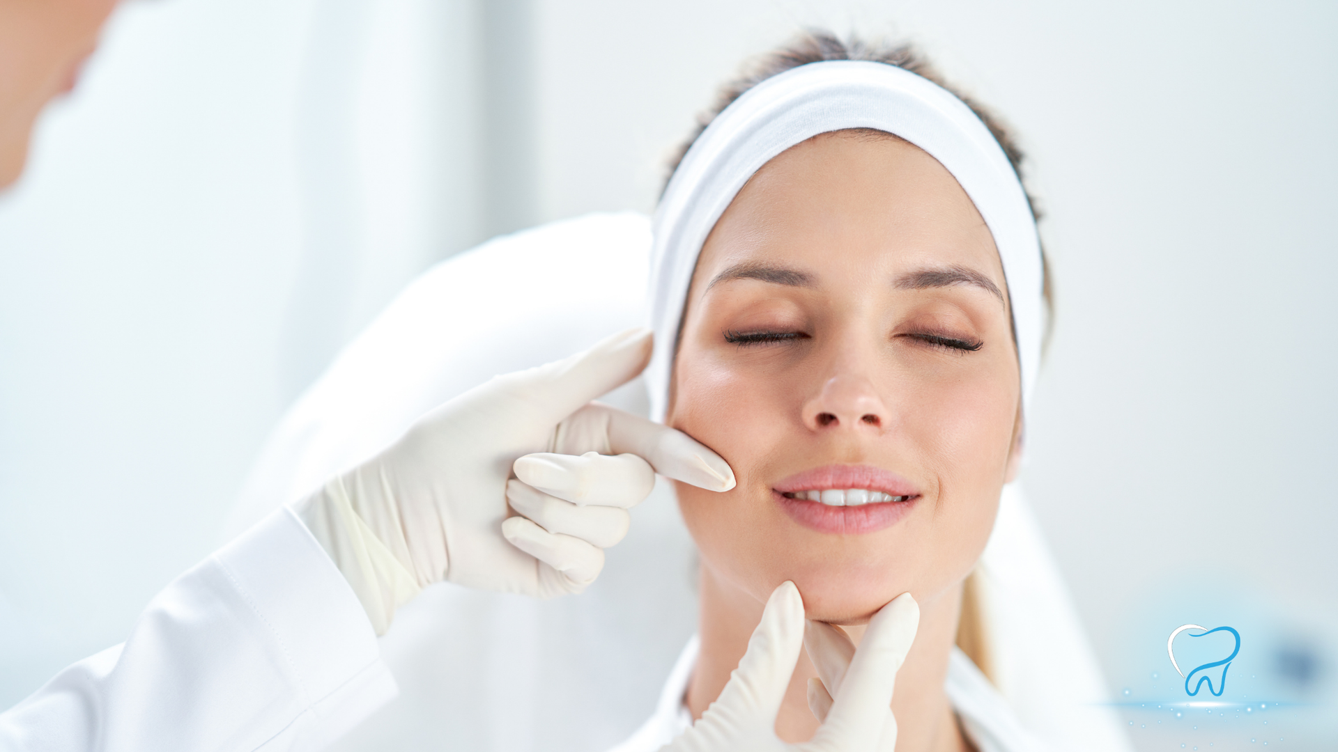 Gloved hands apply facial treatment to a relaxed woman wearing a white headband and towel