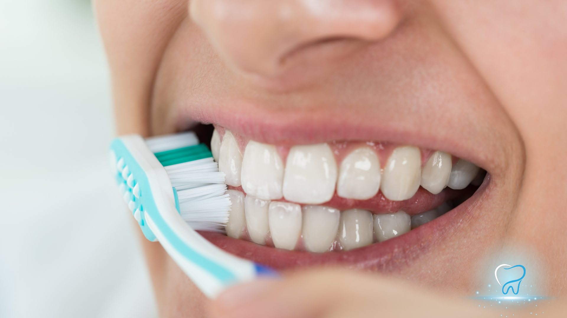 Close-up of a smiling mouth being brushed with a turquoise-and-white toothbrush