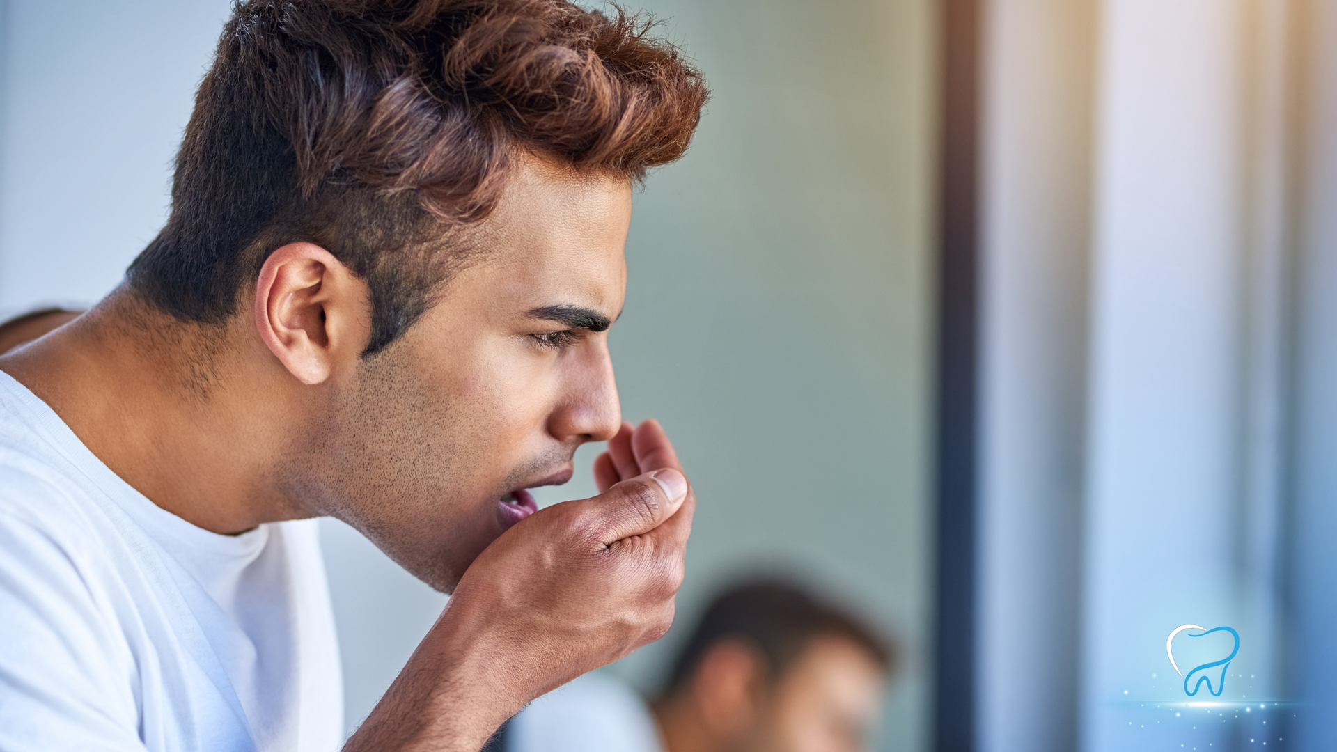 Man smelling a cup in a bright room, with a blurred person in the background