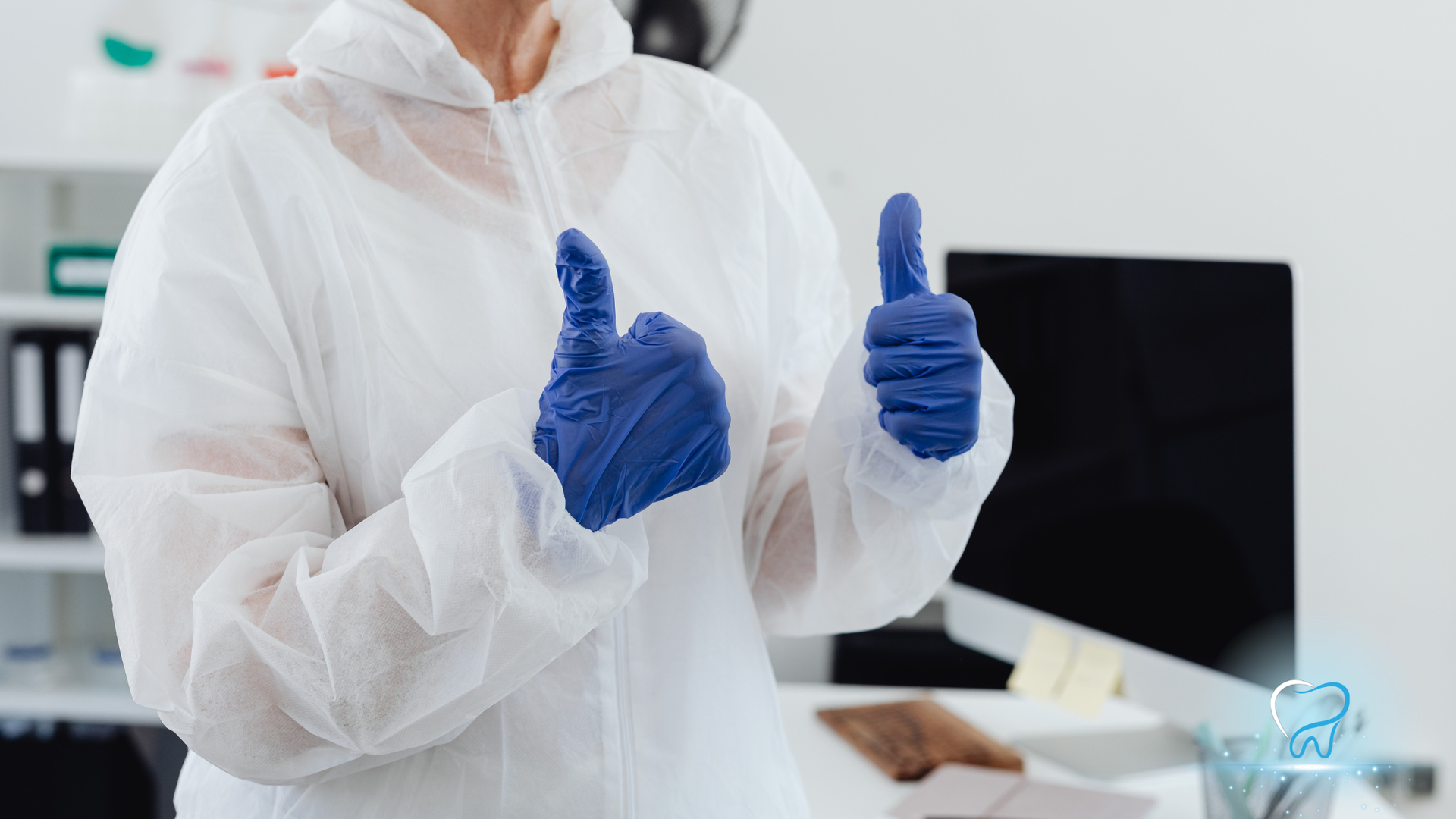 Person in white protective suit and blue gloves giving two thumbs up in an office setting