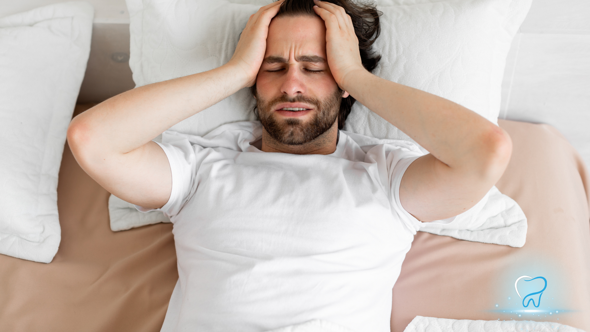 Man lying in bed with hands on his head, looking distressed and in pain