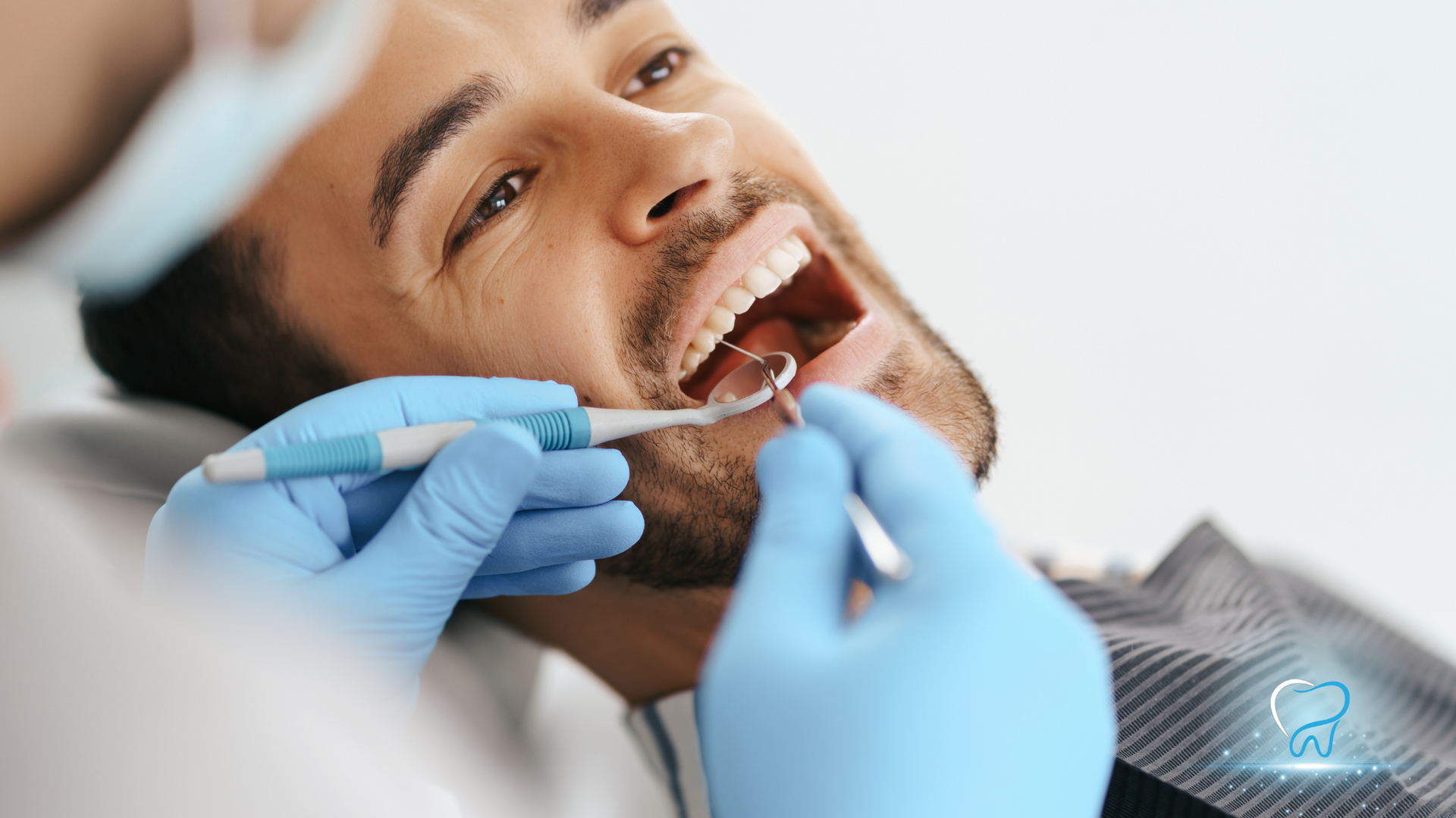 Dentist examining a smiling patient’s teeth with blue-gloved hands and dental tools