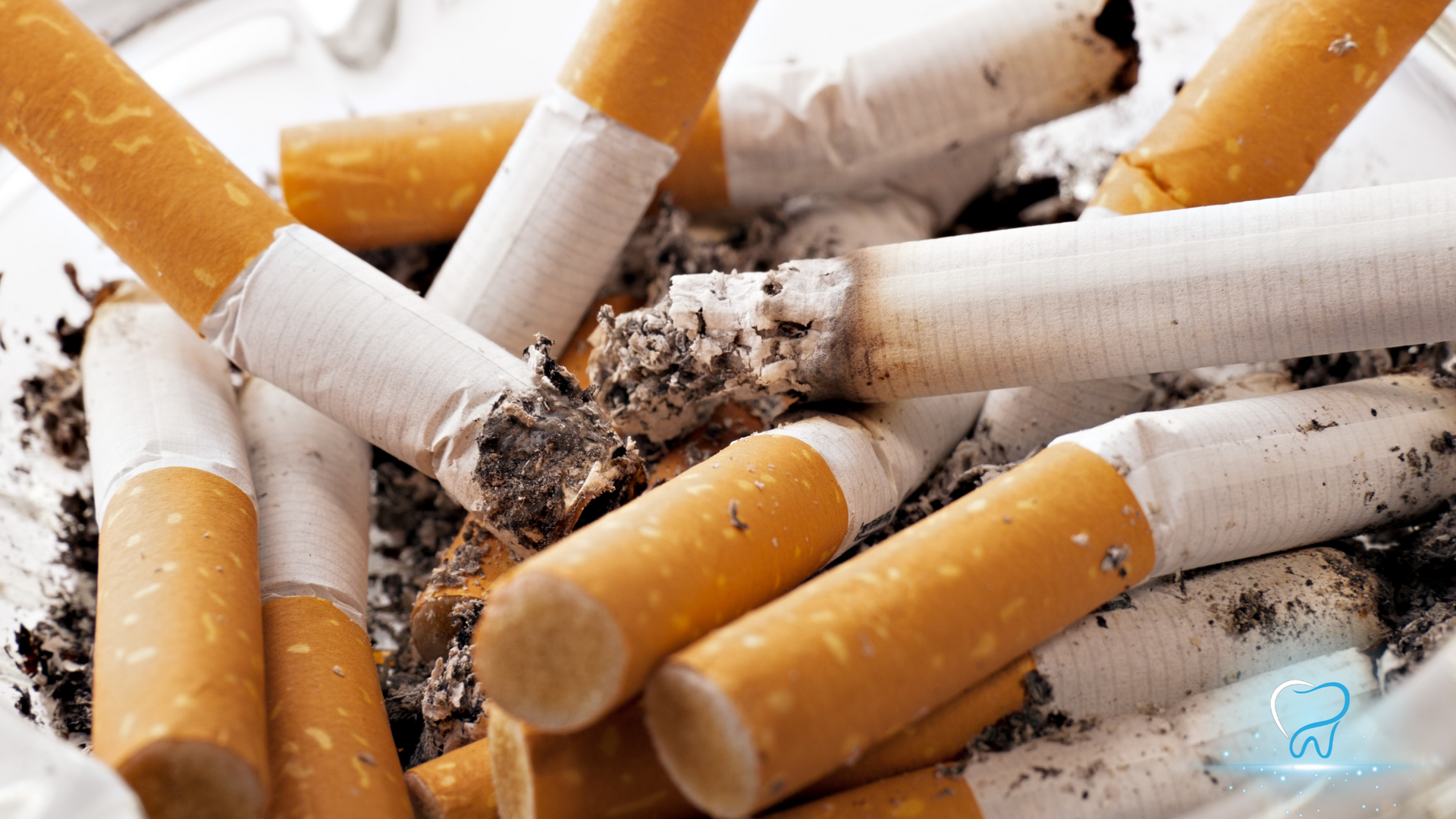 Pile of discarded cigarette butts with ashes and tobacco remnants on a white surface