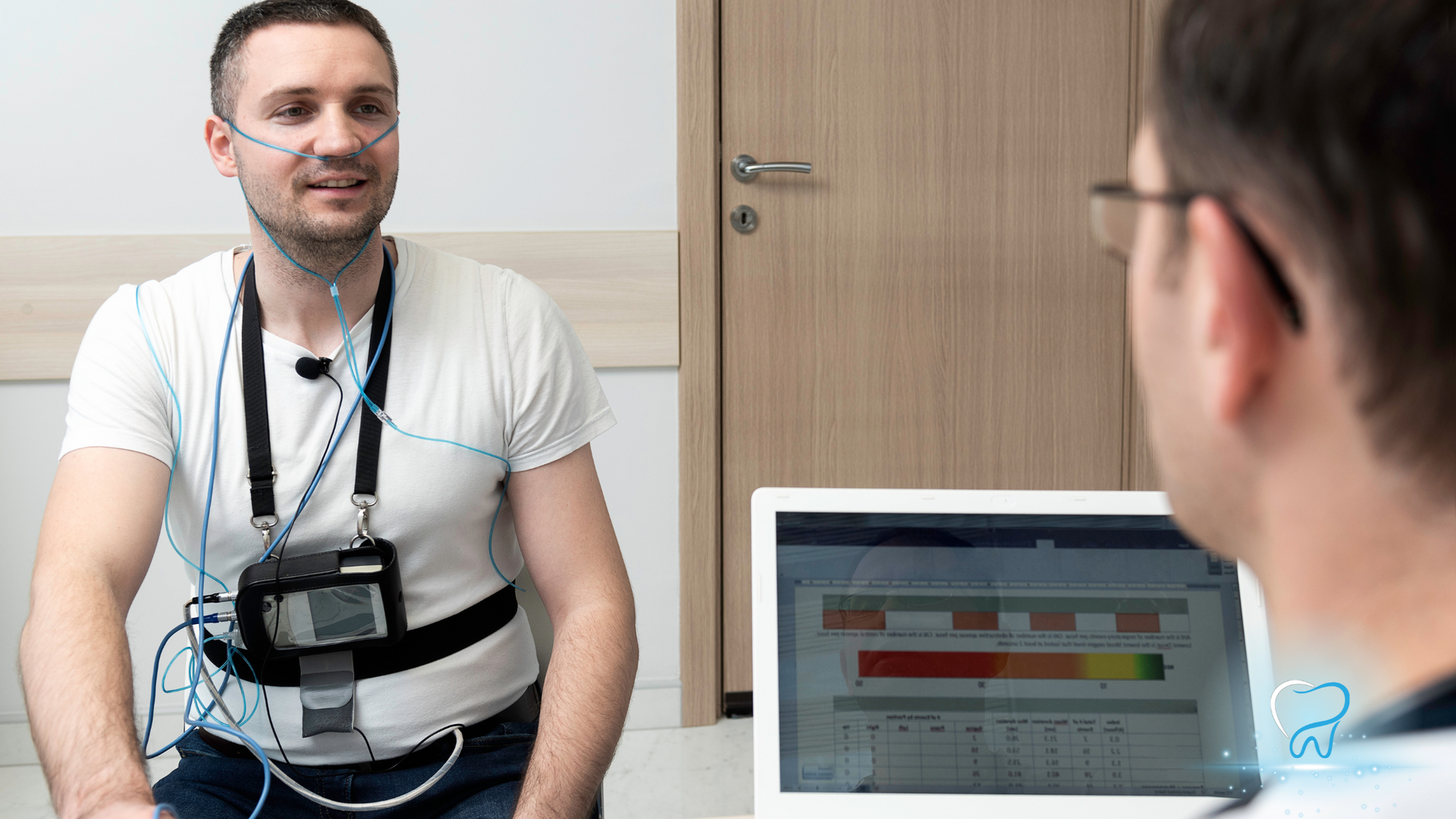 Man sitting in a room with medical sensors attached, facing a laptop screen with charts.
