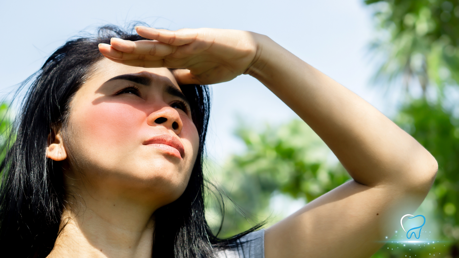 Woman shading her eyes from the sun outdoors, looking upward in bright light
