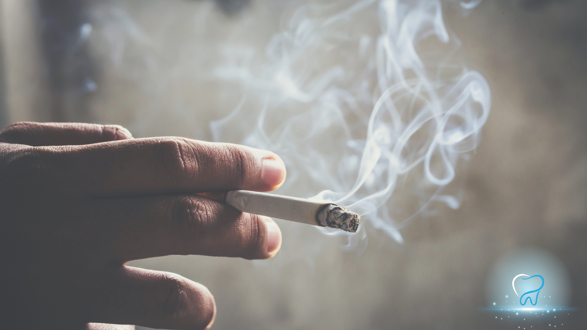 Close-up of a hand holding a lit cigarette with smoke curling into the air.