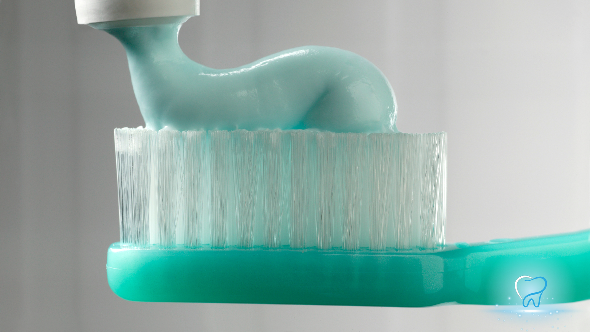 Toothbrush with teal toothpaste being squeezed onto white bristles over a teal base