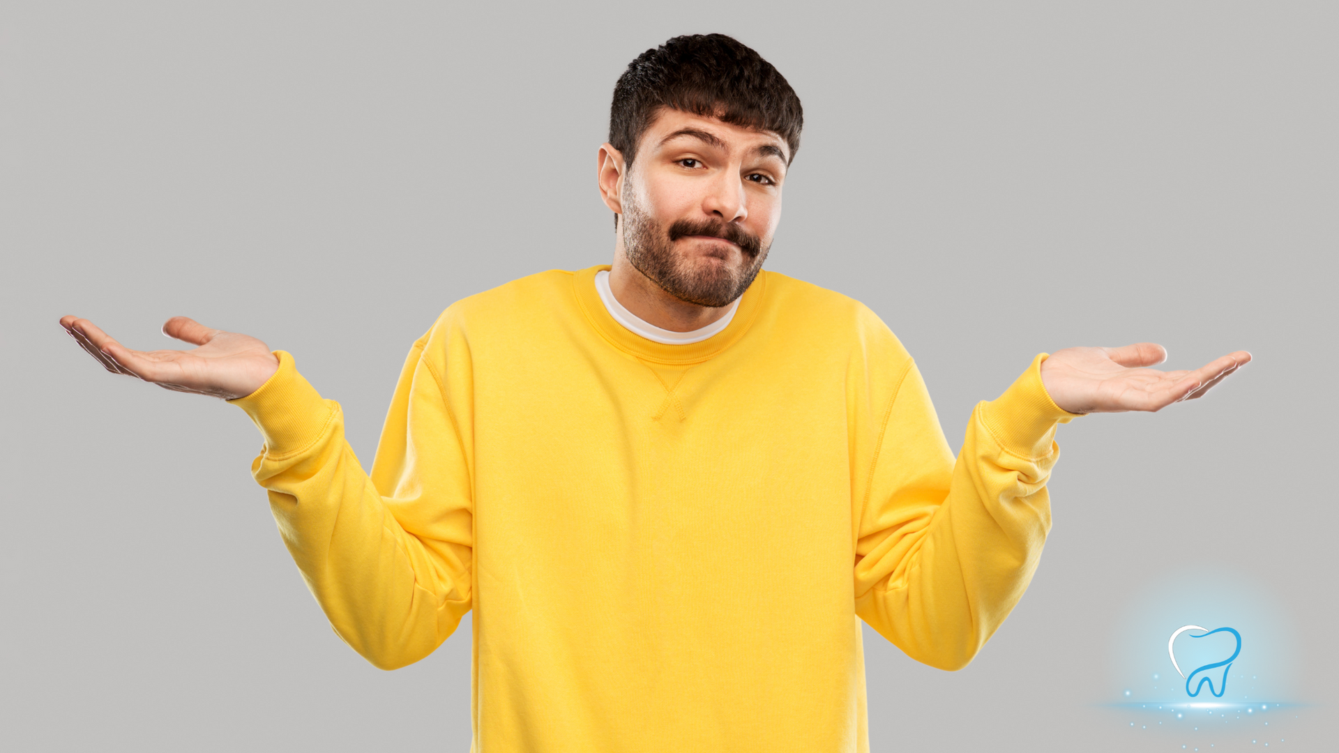 Man in a yellow sweater shrugging with palms up against a gray background