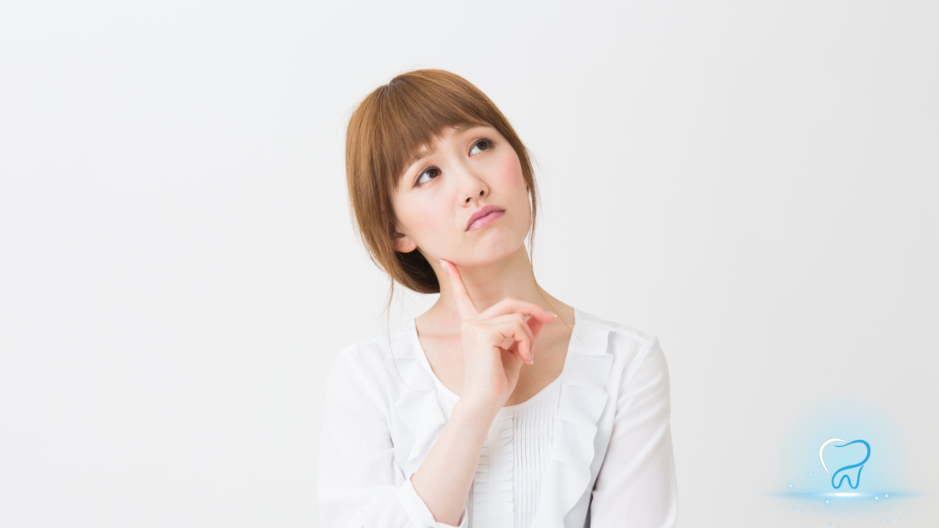 Woman in a white blouse thinking, hand on chin, against a light background.