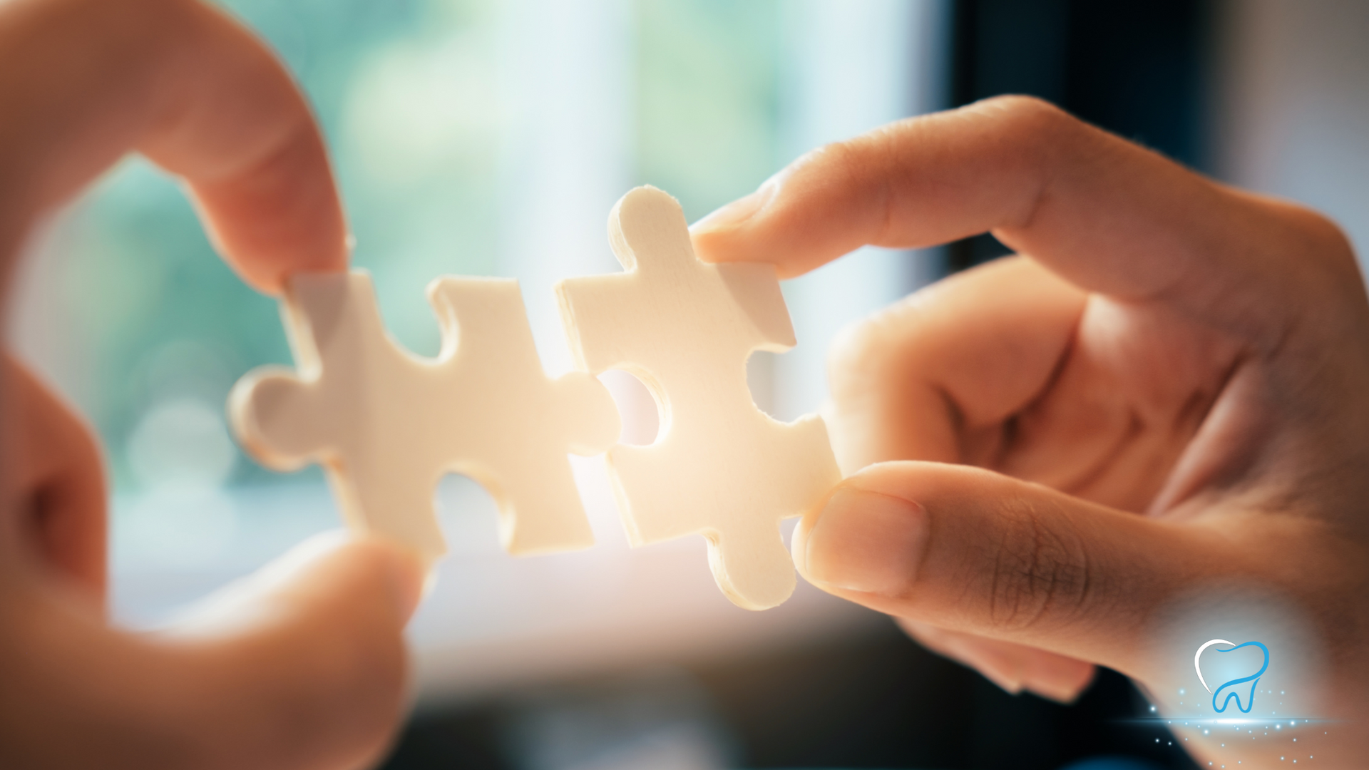 Hands holding together two white puzzle pieces against a warm blurred background.