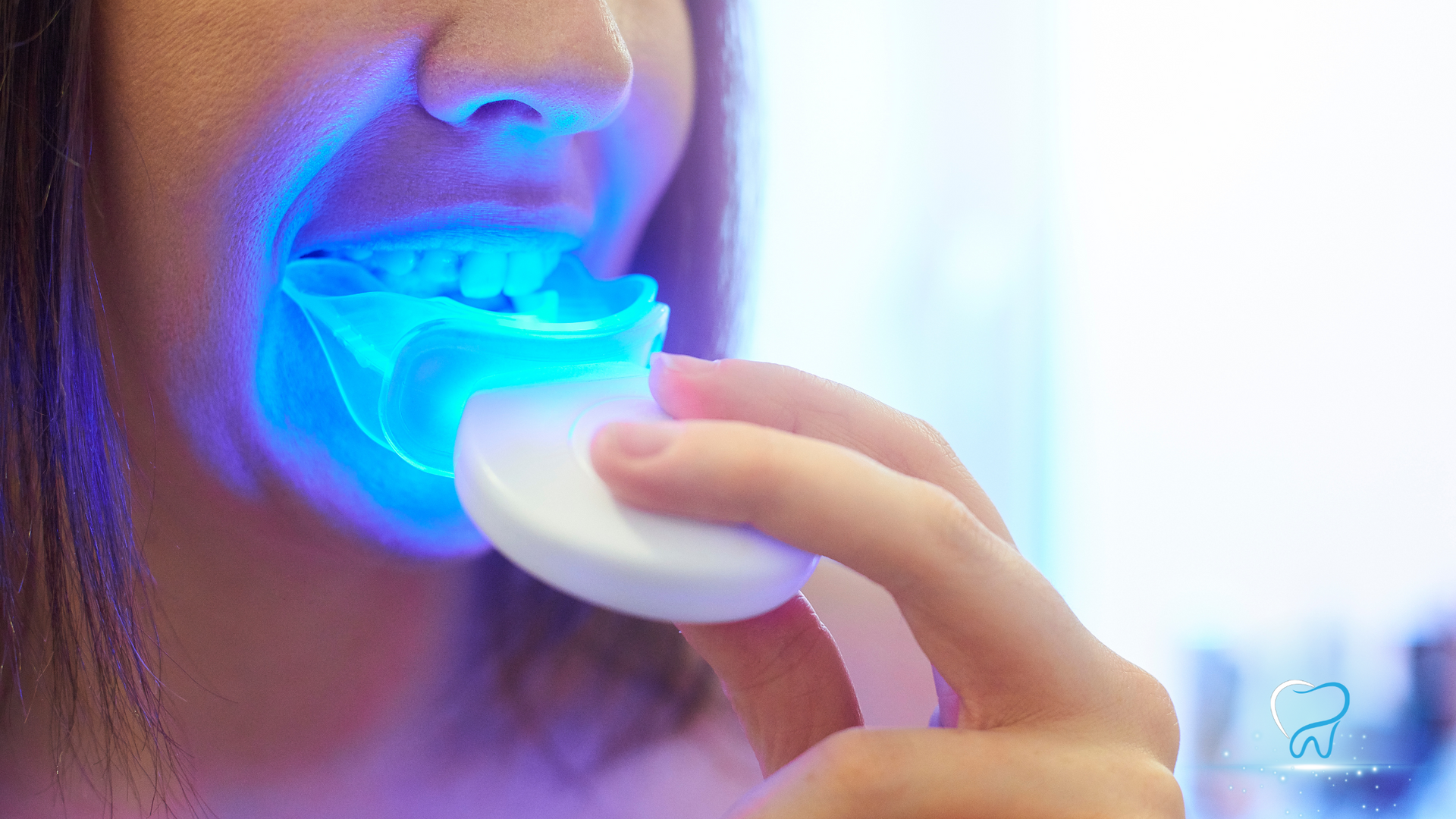 Woman holding a glowing blue LED teeth-whitening mouthpiece to her mouth