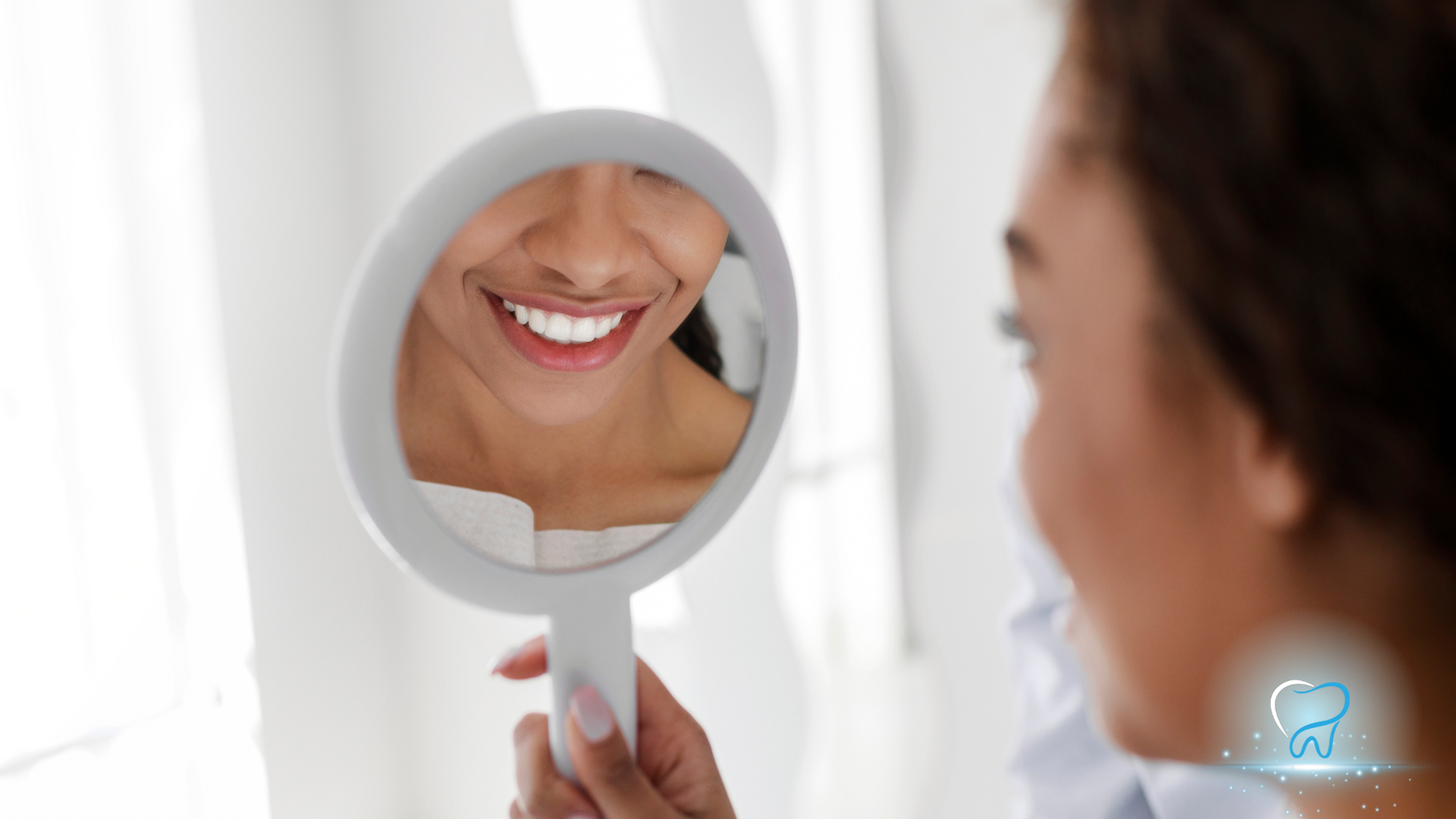 Woman smiling into a handheld mirror, showing her teeth and lips in close-up.