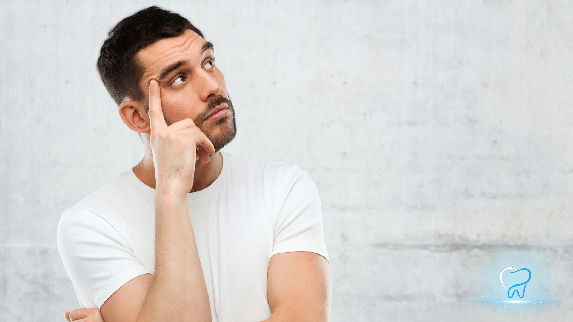 Man in white T-shirt resting his chin on his hand and looking up, against a light gray wall.