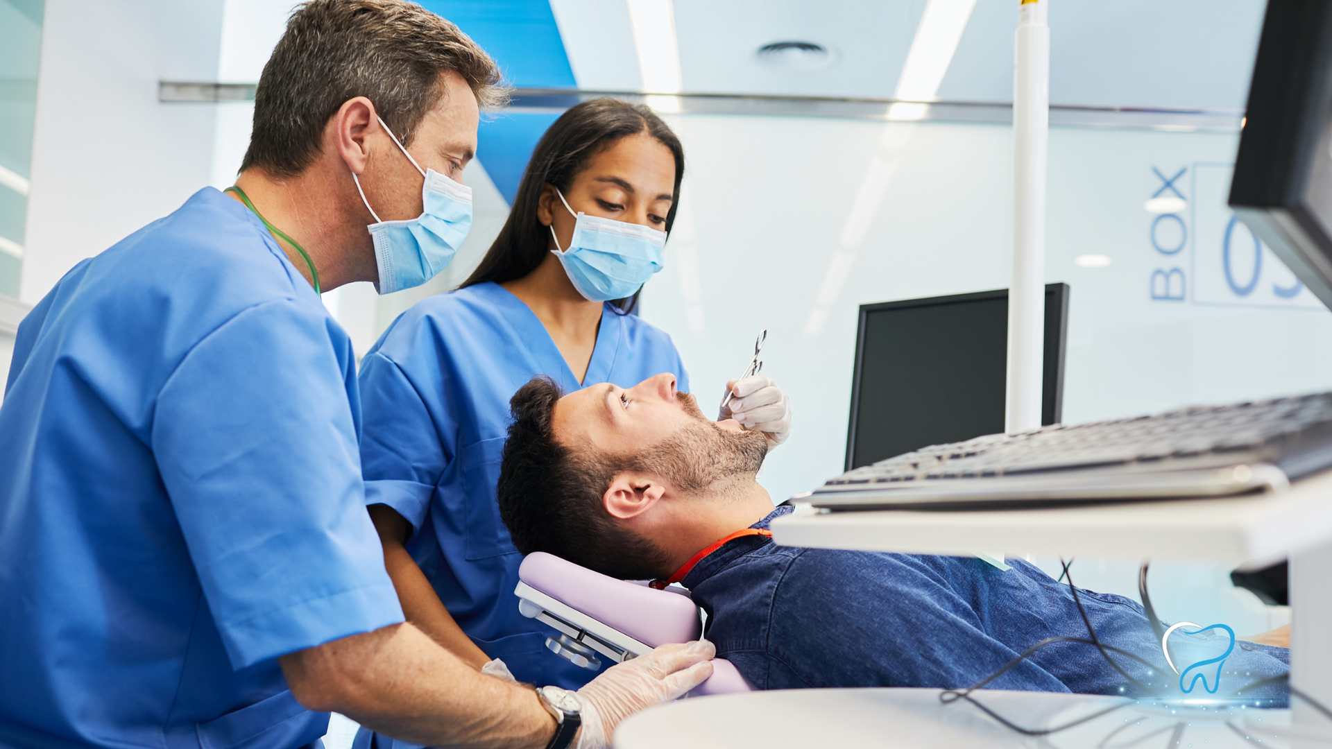 Dental team treating a patient in a clinic, with two masked clinicians around a reclining chair.