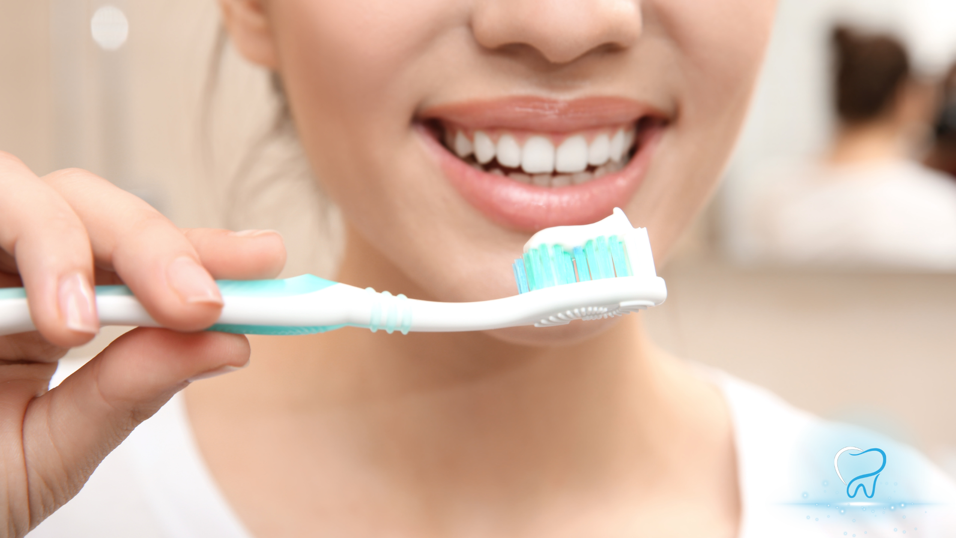 Person brushing teeth with a white and mint toothbrush, smiling in a bathroom.