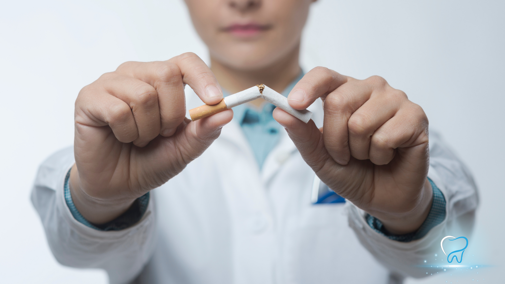 Hands in a white lab coat holding a broken cigarette, symbolizing smoking cessation.