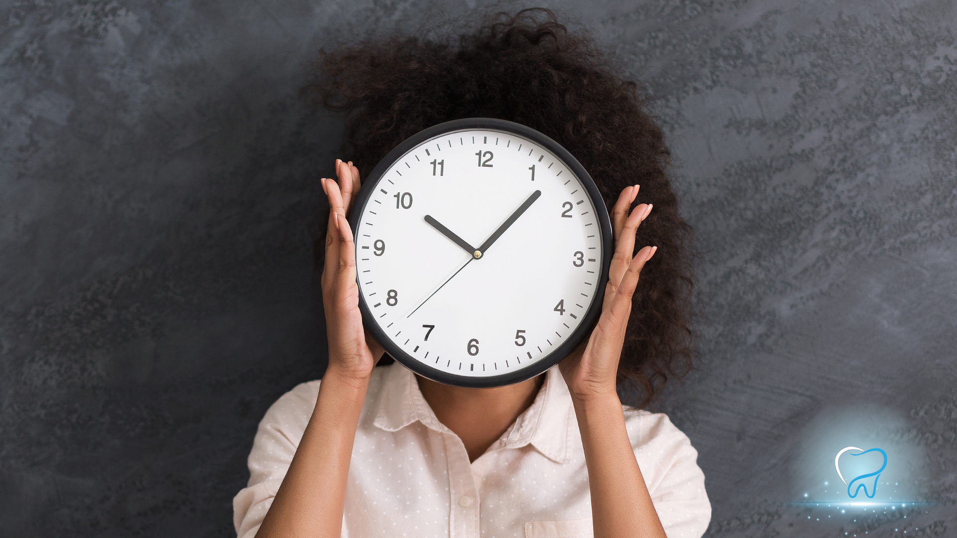 Person holding a wall clock over their face against a dark background.