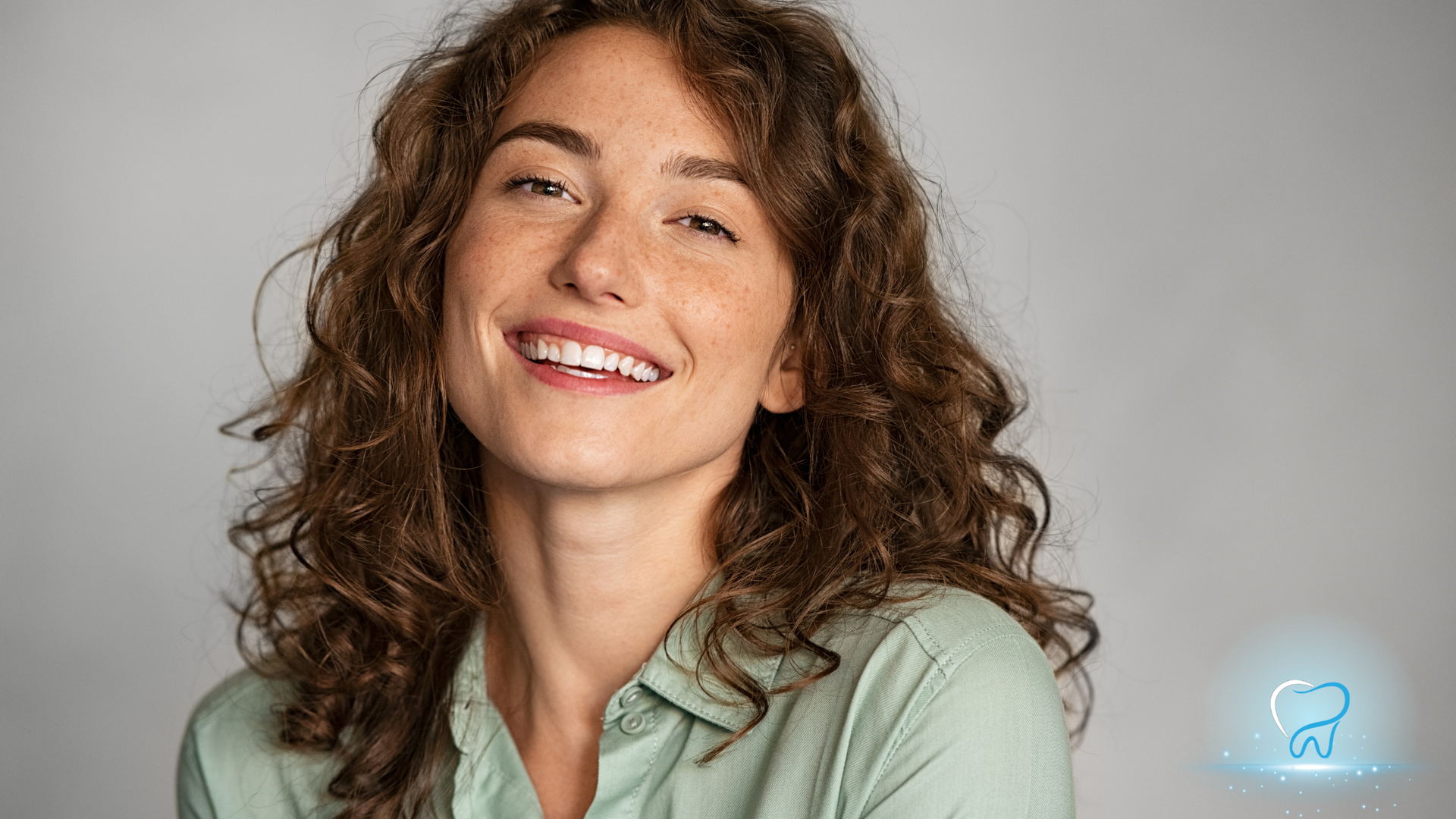 Smiling person with curly brown hair in a light green shirt against a gray background