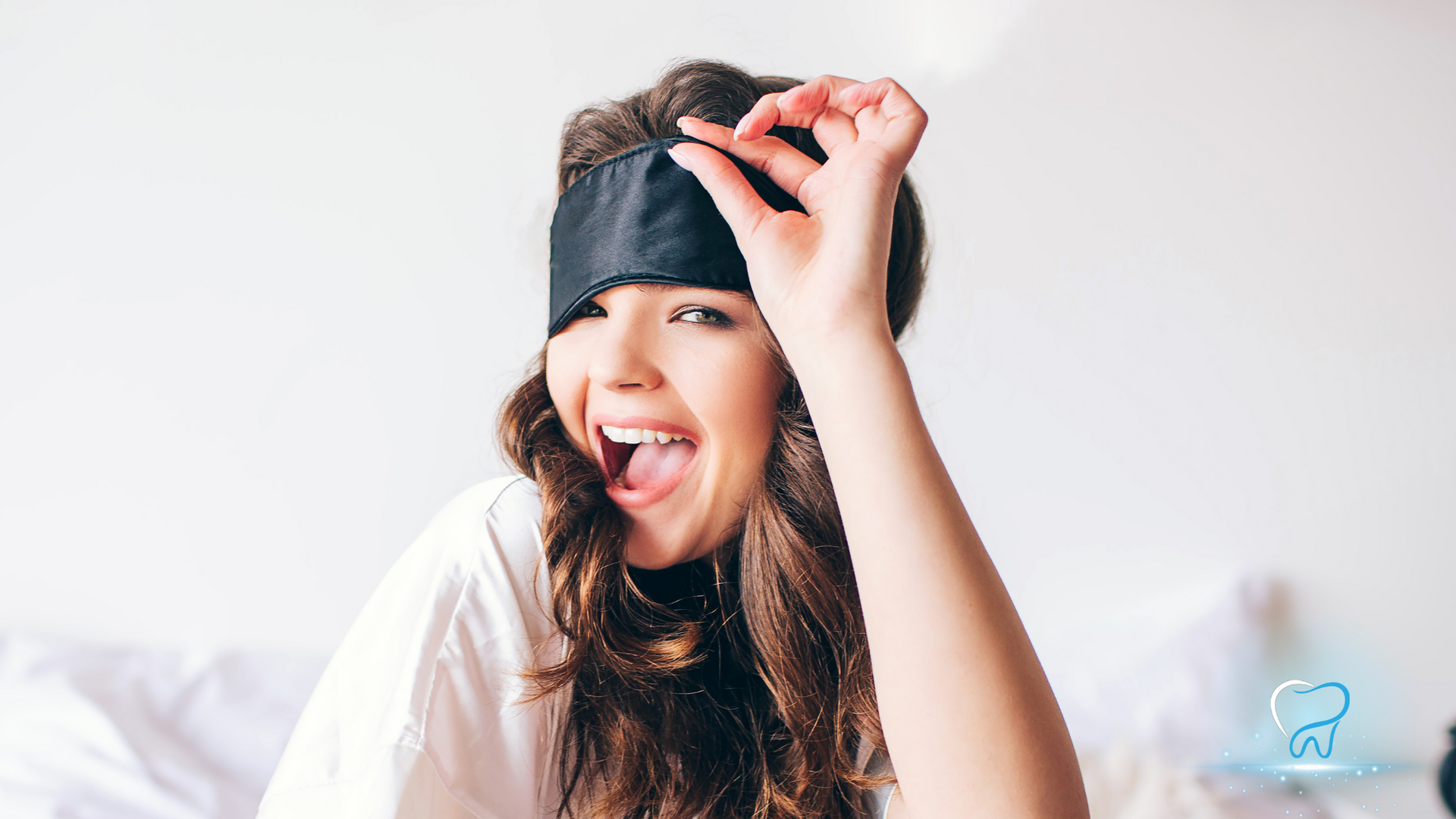 Smiling woman wearing a black blindfold, raising one hand against a bright white background