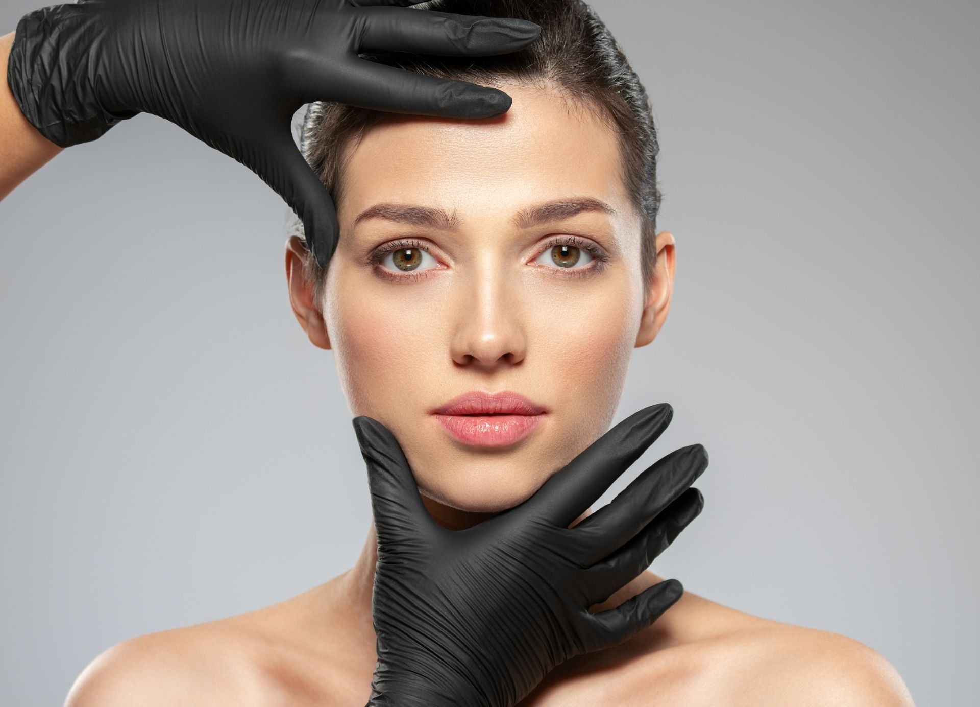 Gloved hands framing a woman’s face against a gray background