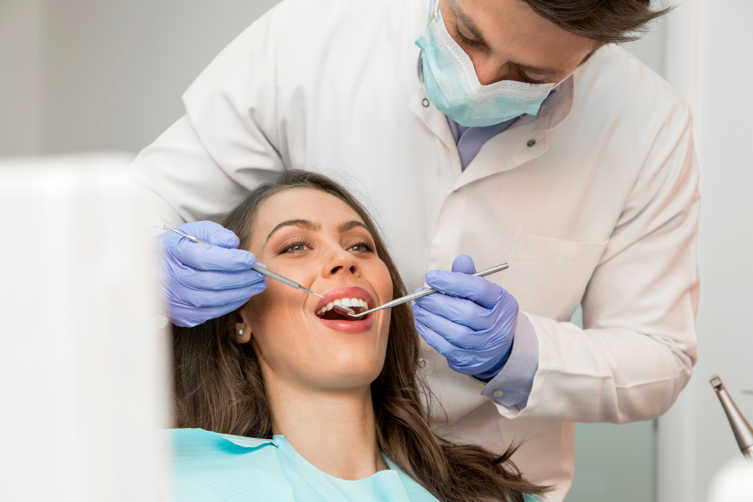 Dentist examining a smiling patient’s teeth in a bright clinic