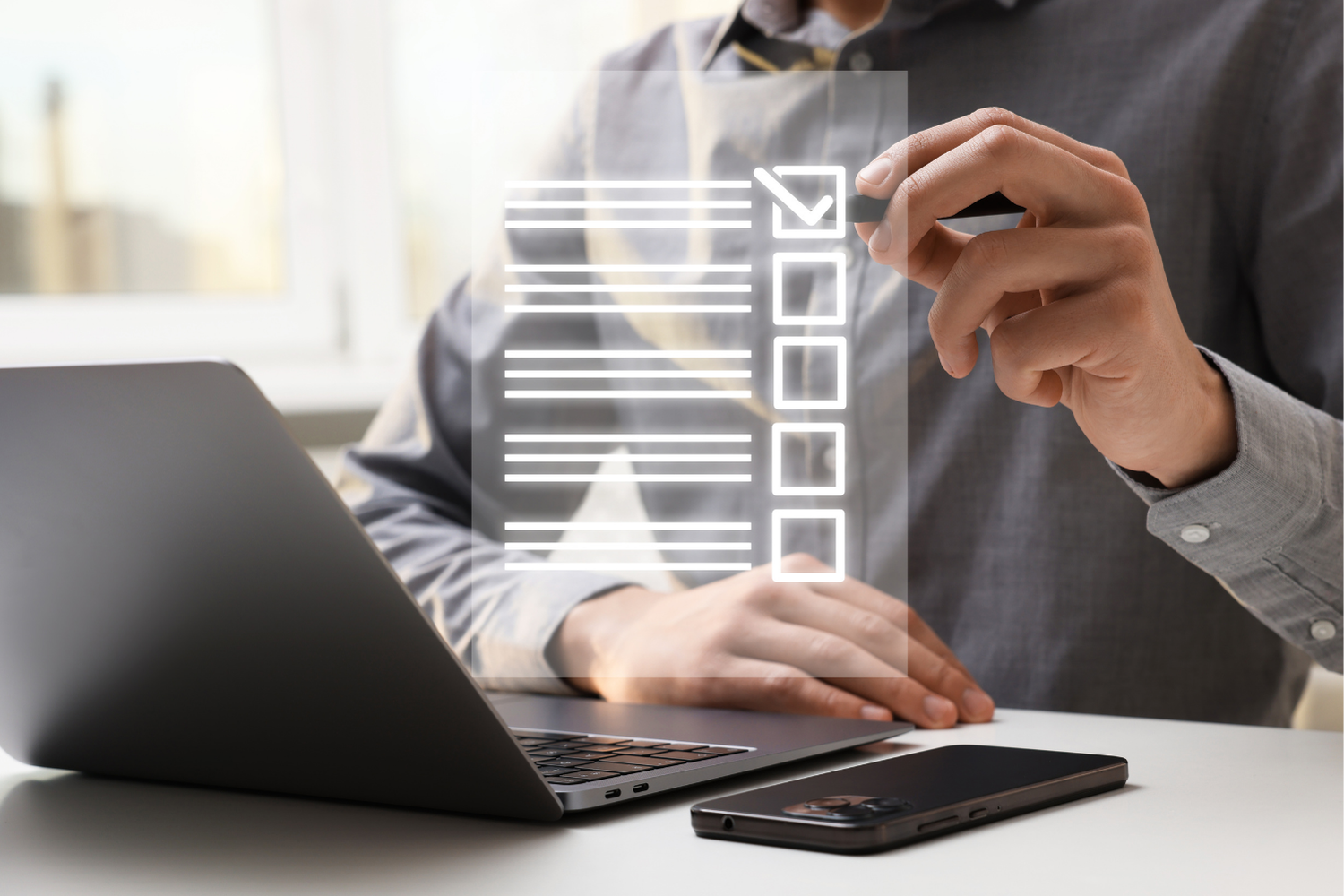 Person using a laptop and tapping a digital checklist interface above a smartphone on a desk