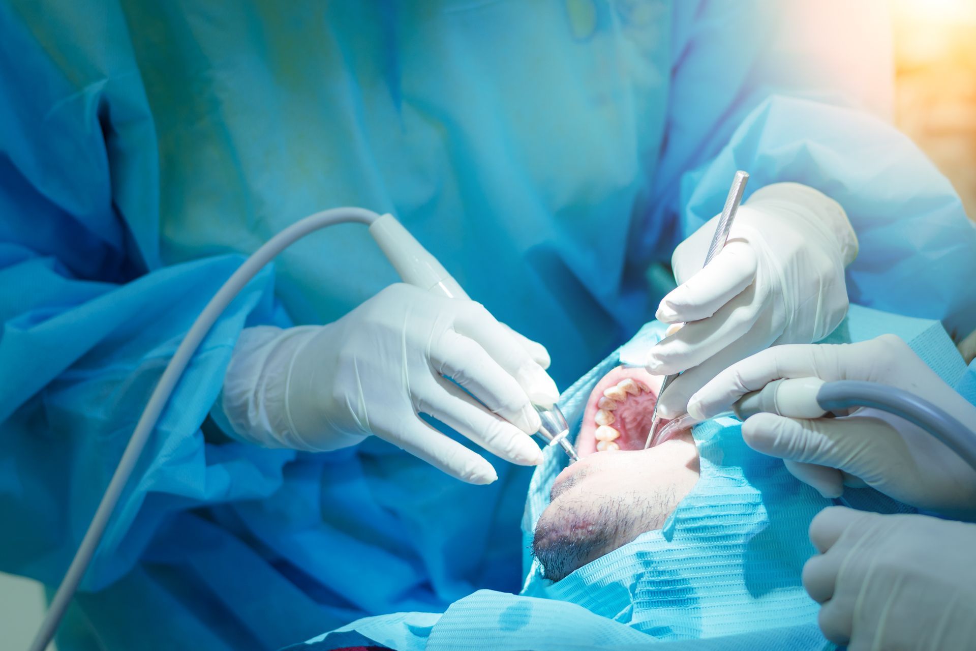 Surgeons in blue gowns and gloves performing an operation in a bright operating room
