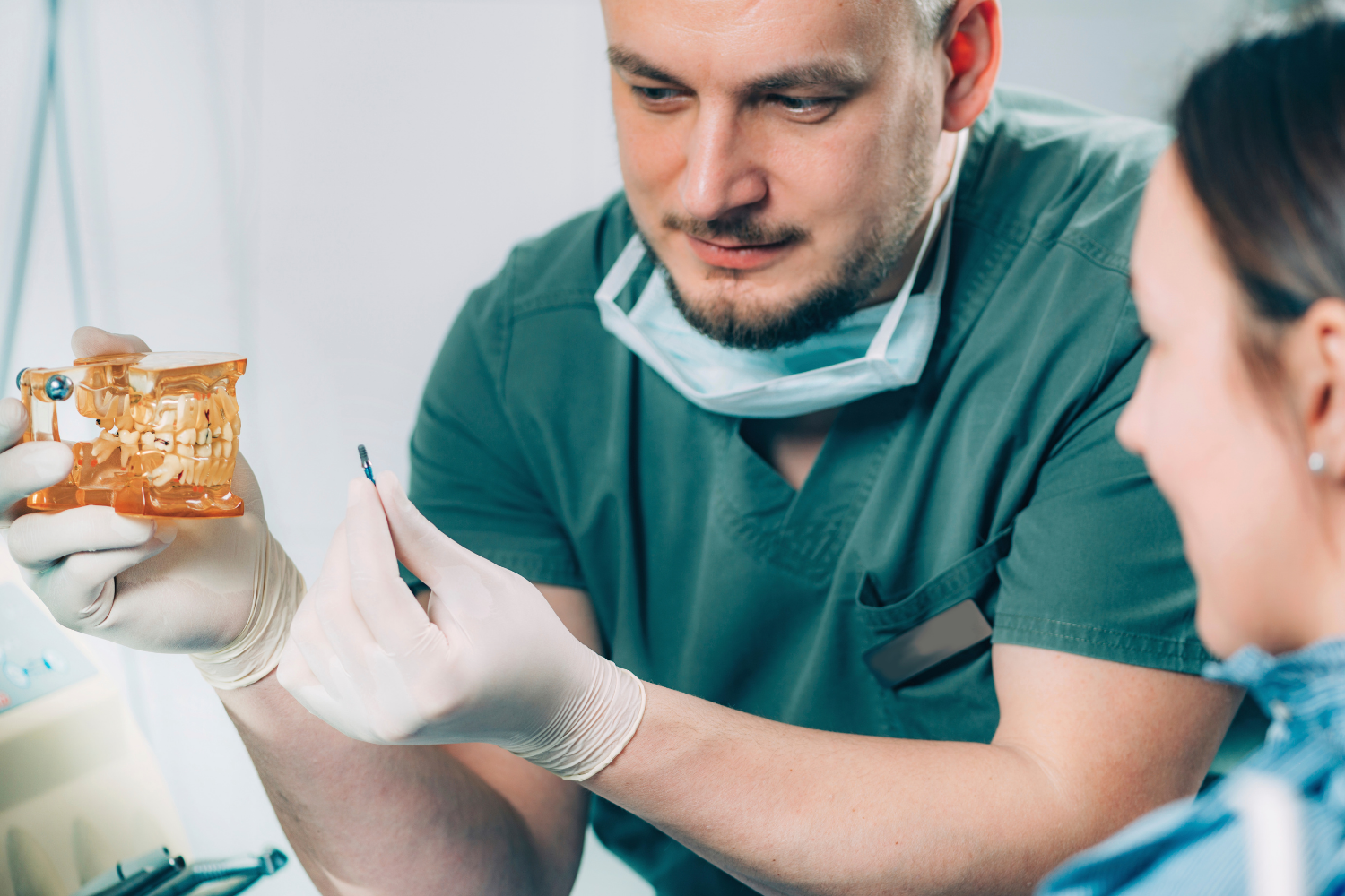 Dentist and assistant examining a dental mold in a clinic, wearing gloves and scrubs.
