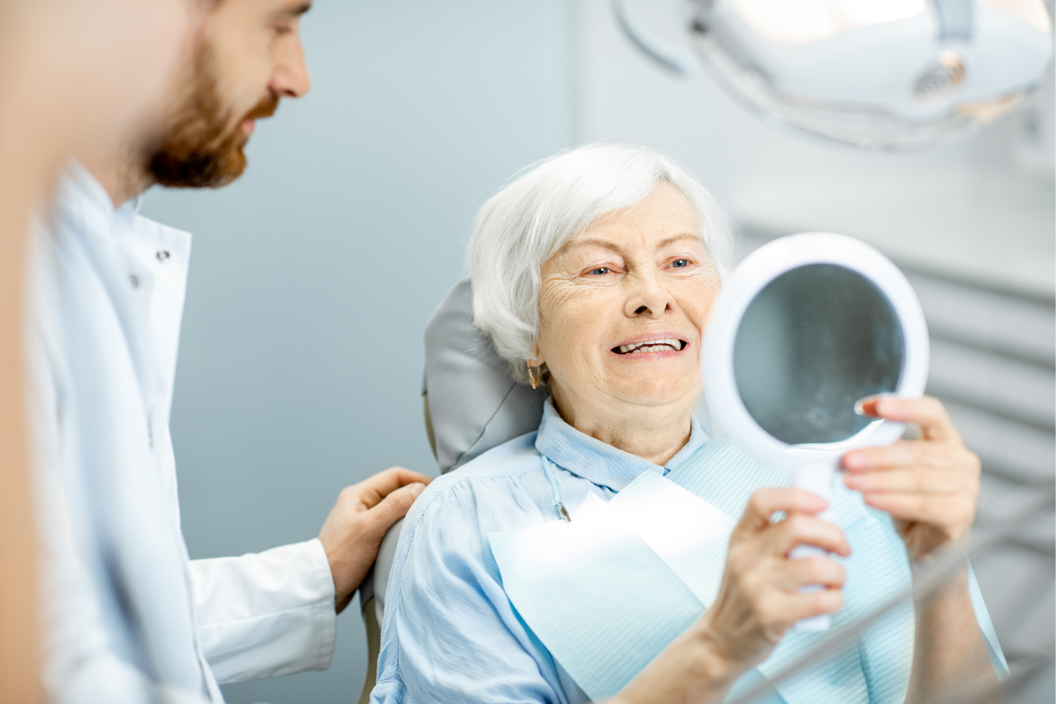 Dentist assisting patient holding a dental mirror in a bright clinic