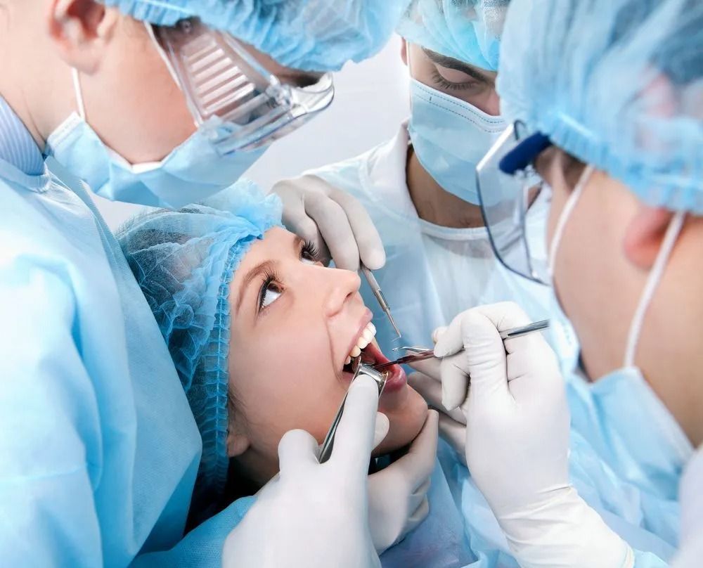 Dentists in blue surgical gear treating a patient’s mouth in a clinical setting