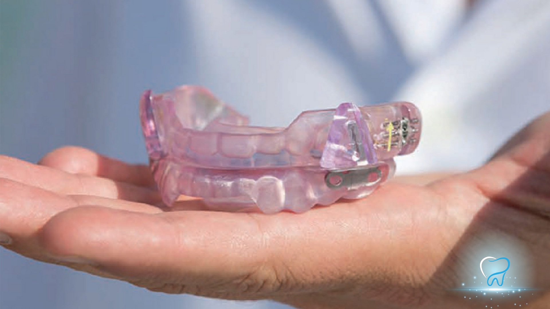 Hand holding a transparent pink dental mouth guard against a bright background