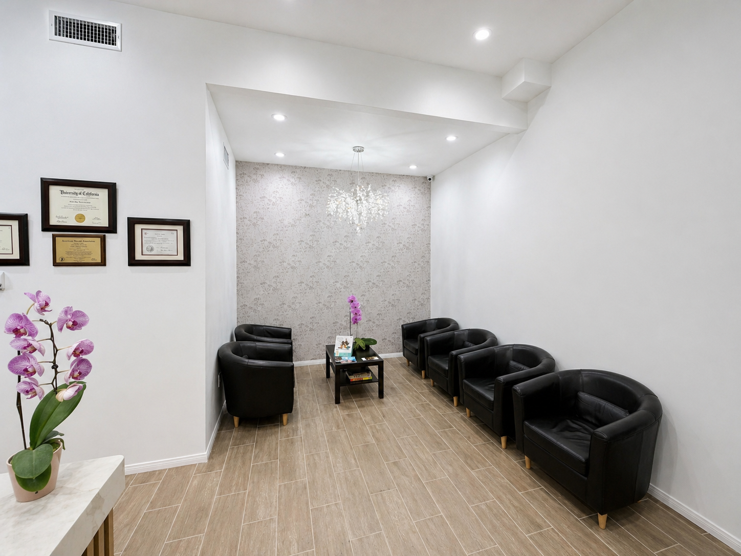 Bright waiting room with black chairs, white walls, wood floor, and purple orchid decor.