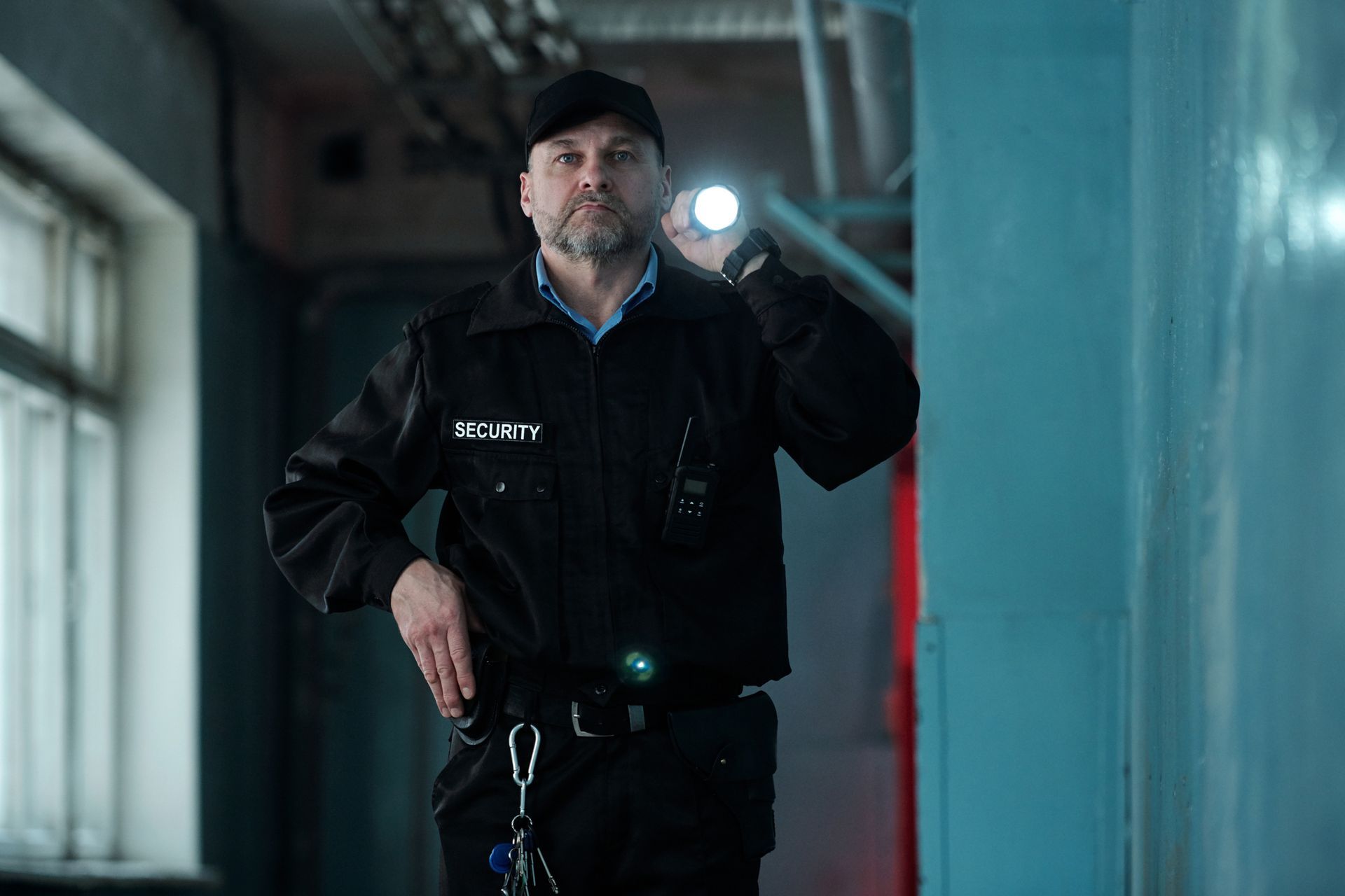 Security guard in dark uniform holding flashlight, inspecting a hallway.