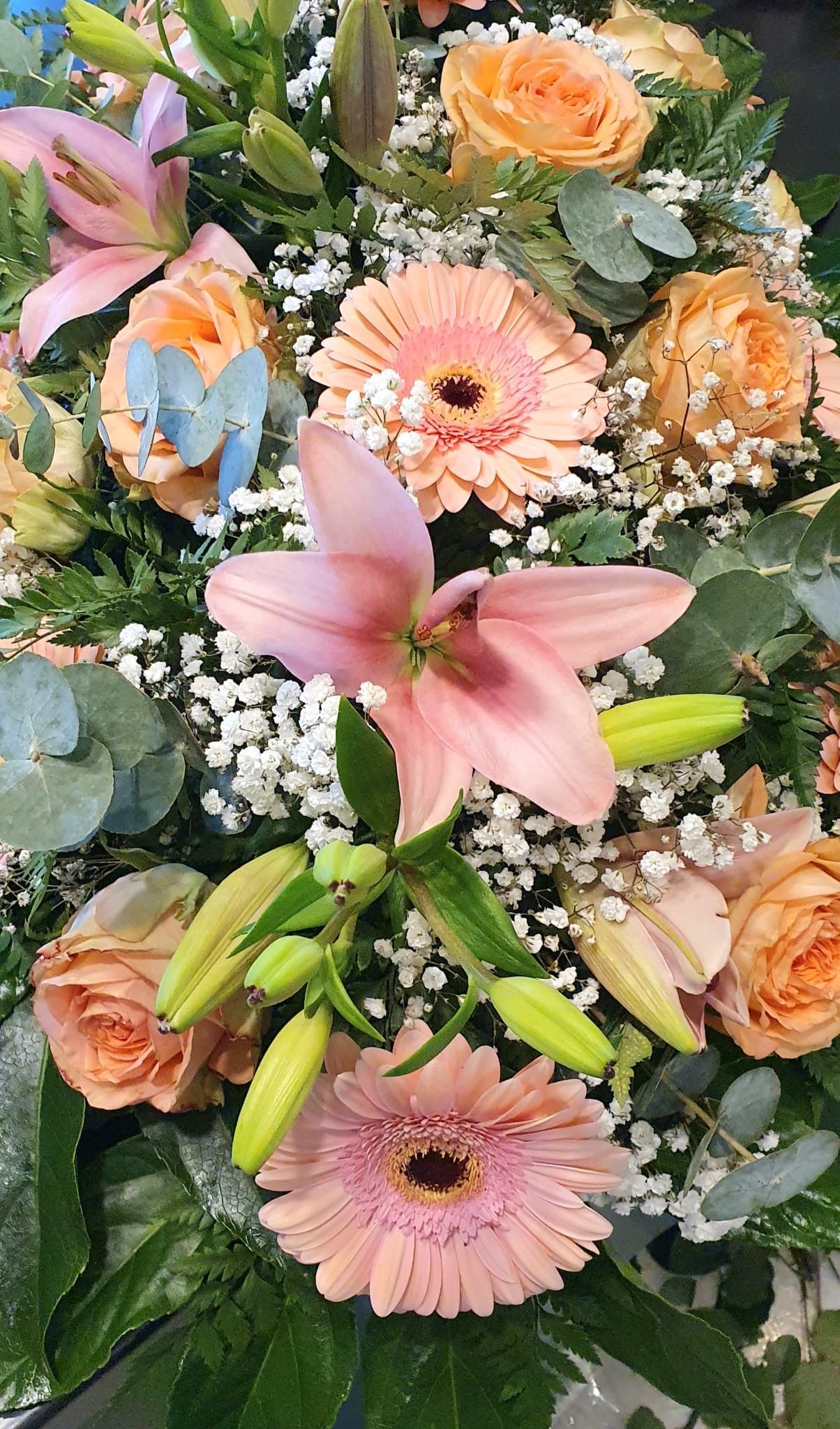 Primo piano di una composizione floreale con gigli rosa, rose color pesca e gerbere rosa.