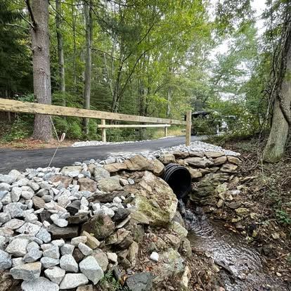 Driveway culvert installation with a stone headwall and riprap by Elevated Excavation