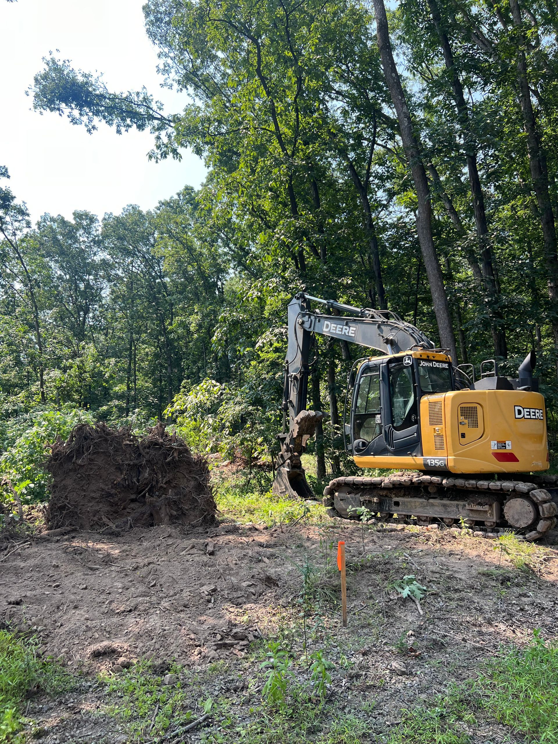 Excavator leveling red dirt on a construction site with trees in the background