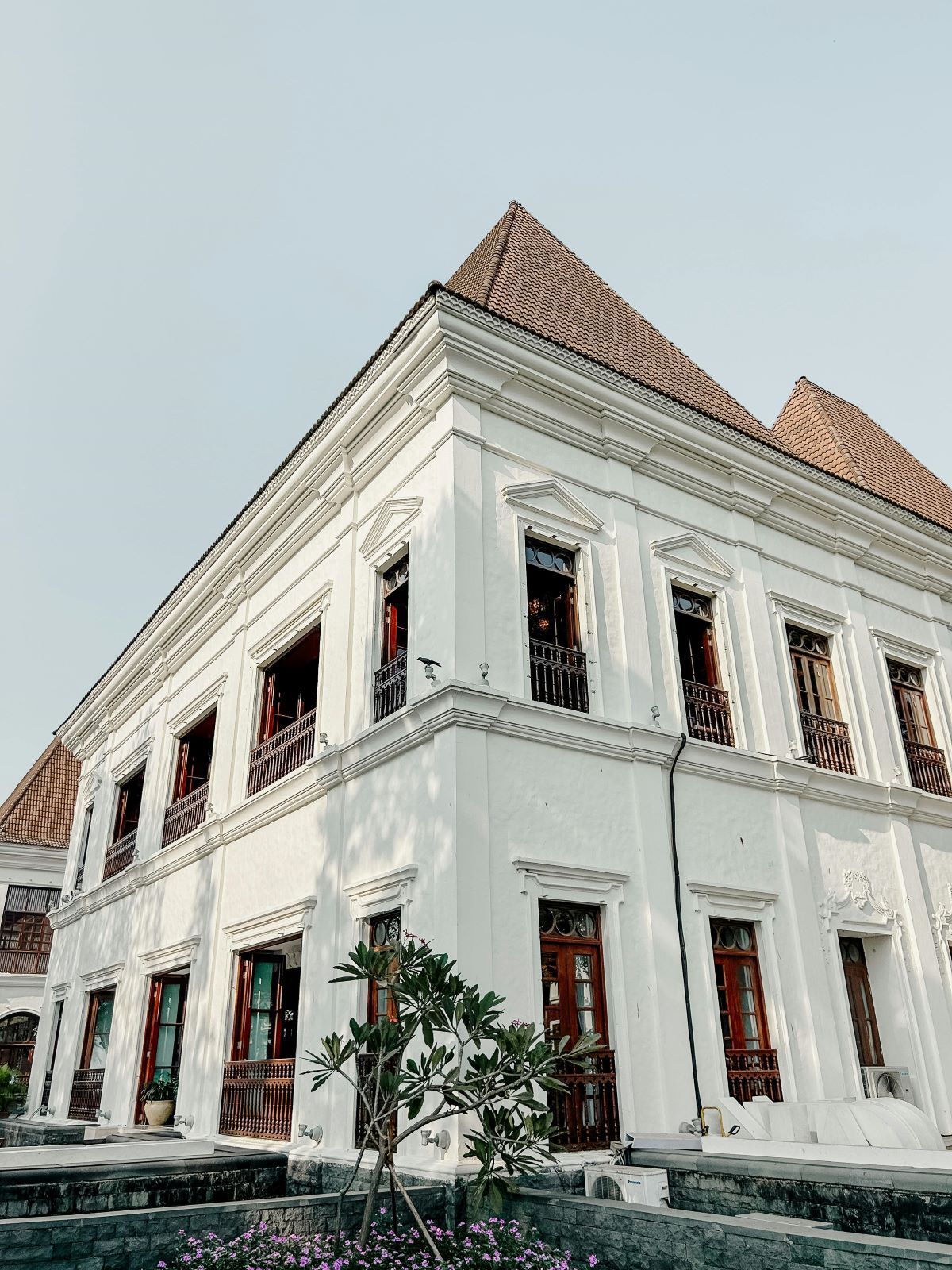 White two-story historic building with a tiled roof and red-trimmed windows against a clear sky