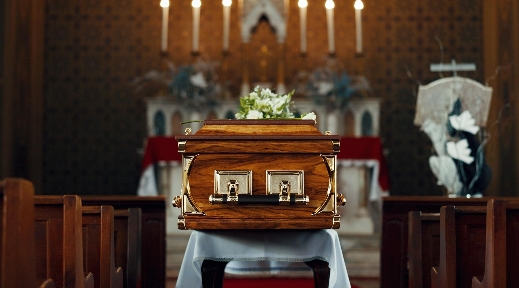 Wooden casket with flowers on a church pew in front of candles and altar