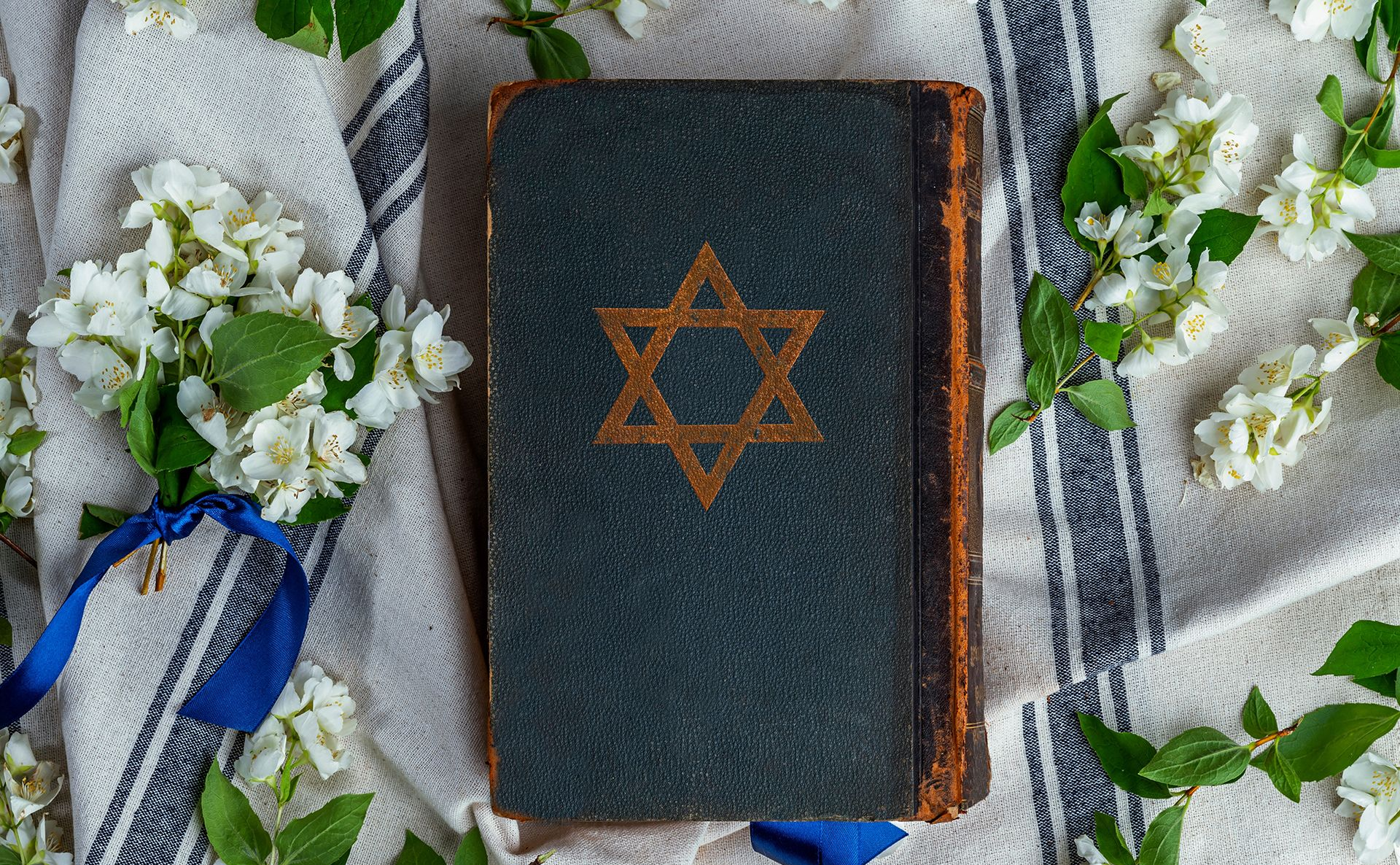 Black notebook with a gold Star of David, surrounded by white flowers on a striped cloth.