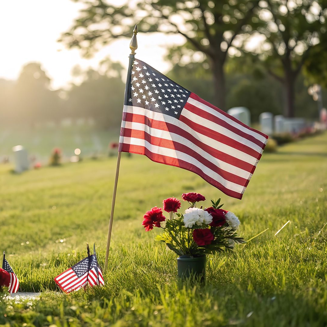 American flags and red-white flowers at a gravesite on a sunny day