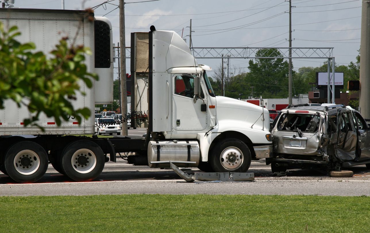 A semi truck is driving down the road next to a damaged car.