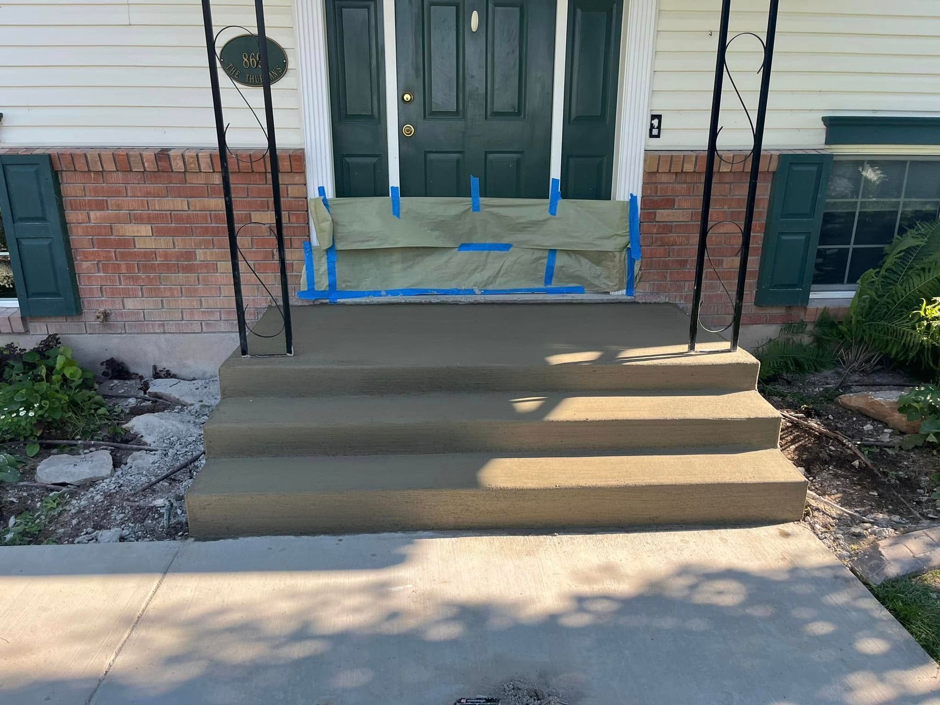Newly poured concrete steps leading to a dark green front door, with protective tape and paper masking the door frame.