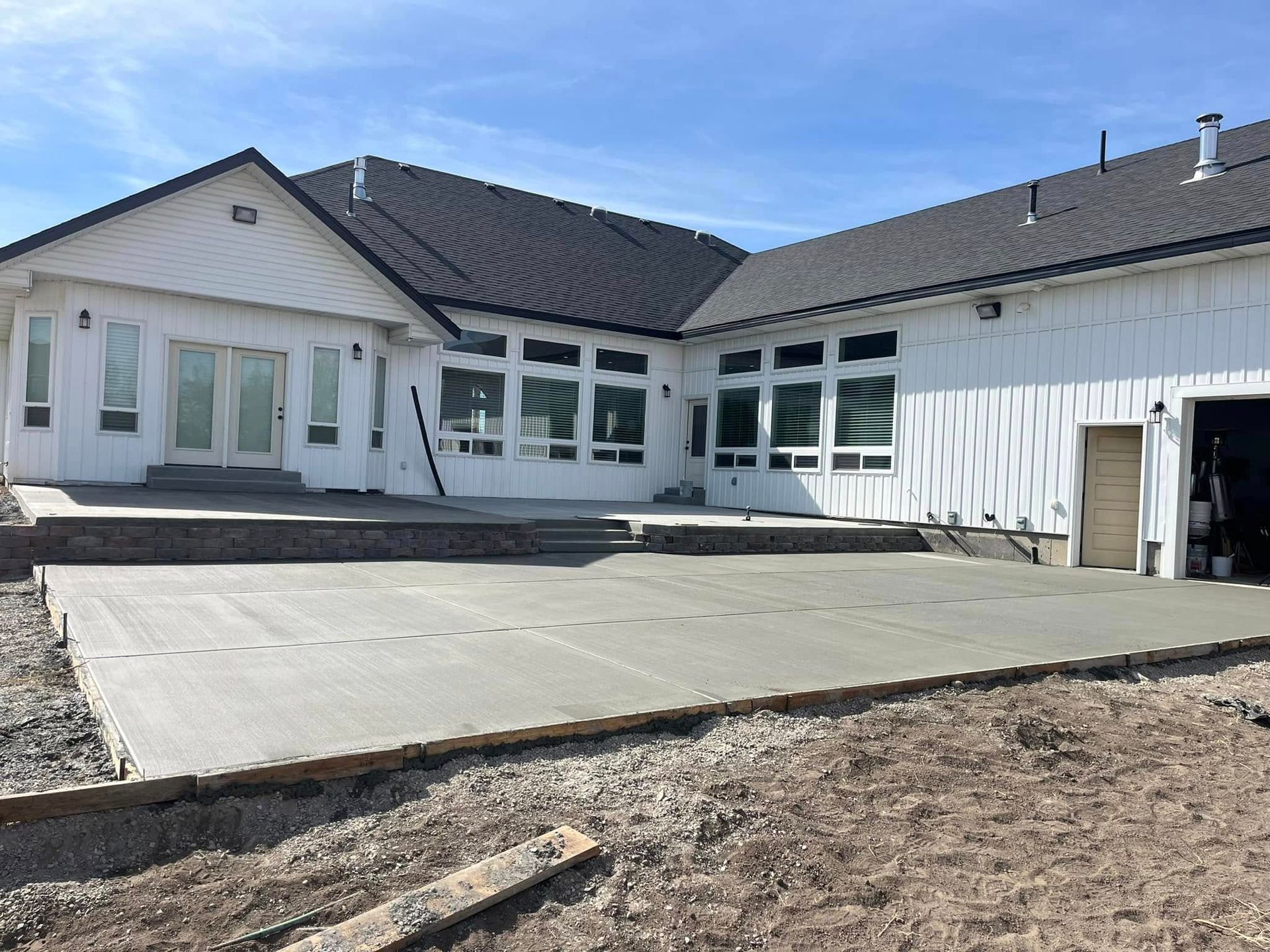 A newly poured concrete patio attached to the back of a large, white house with a dark roof and many windows.