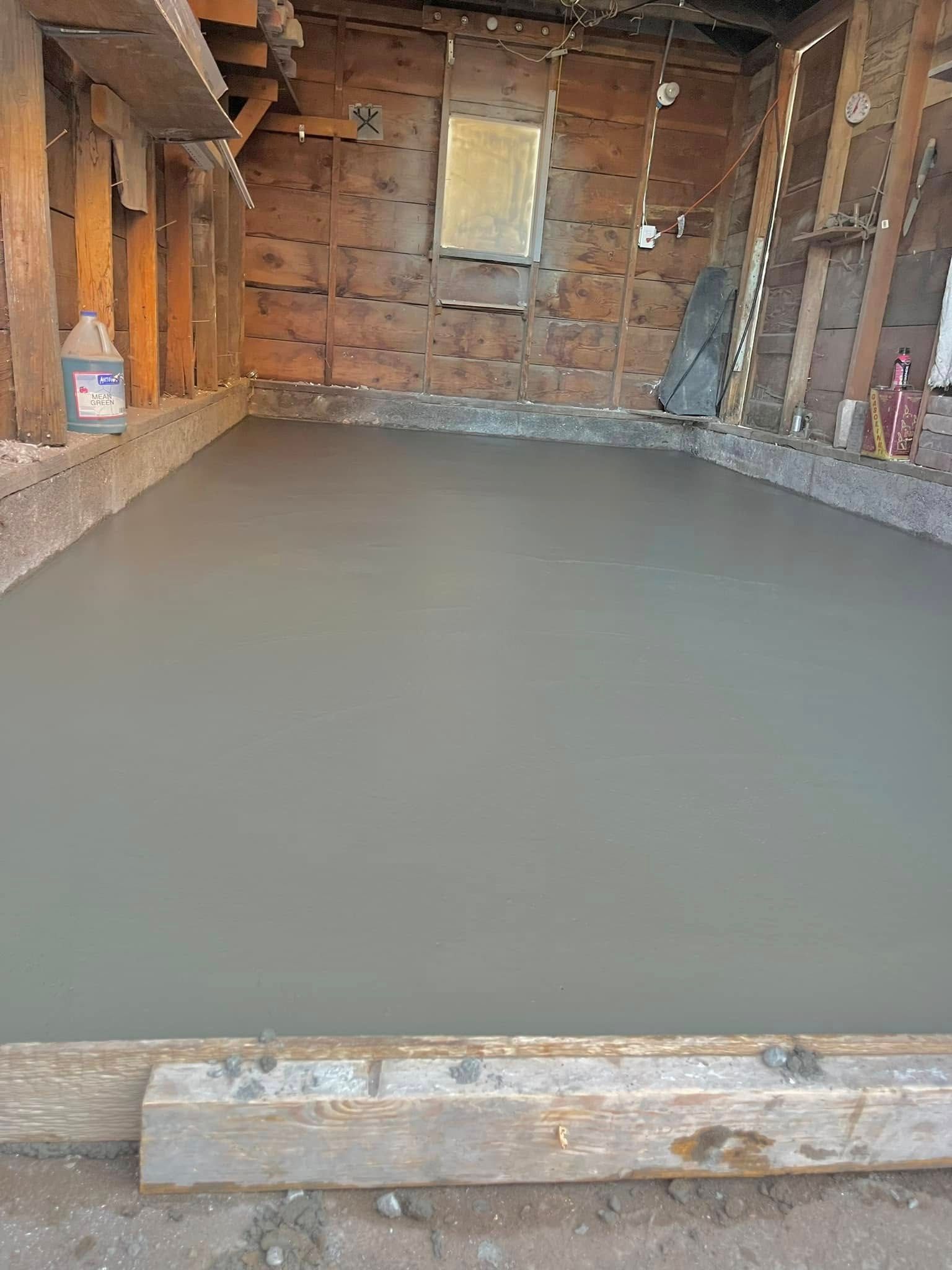 A freshly poured, smooth gray concrete floor inside a framed, unfinished wooden garage structure.