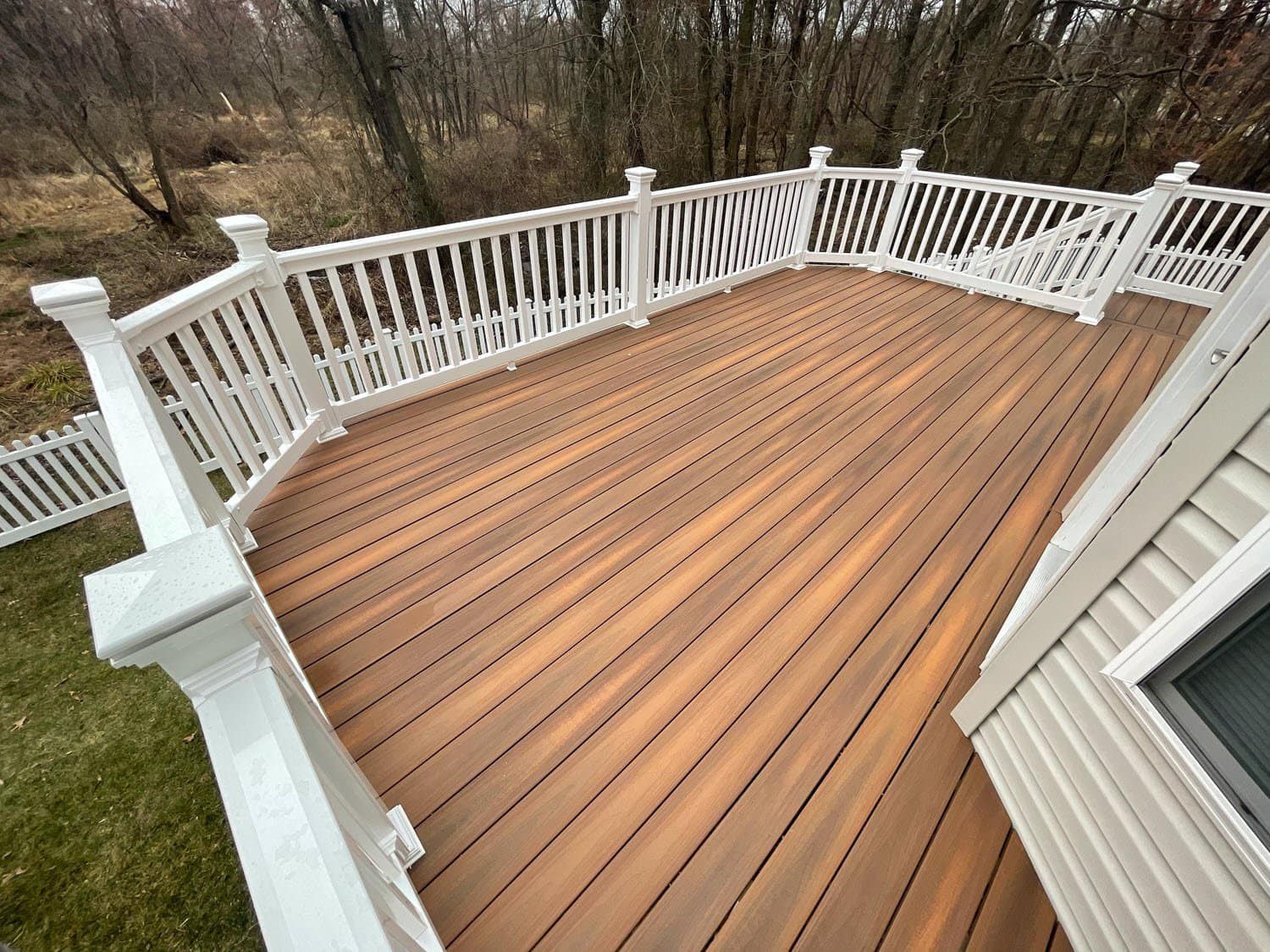 An elevated wooden deck with white railings, looking out over a grassy yard and trees in an autumn or winter setting.