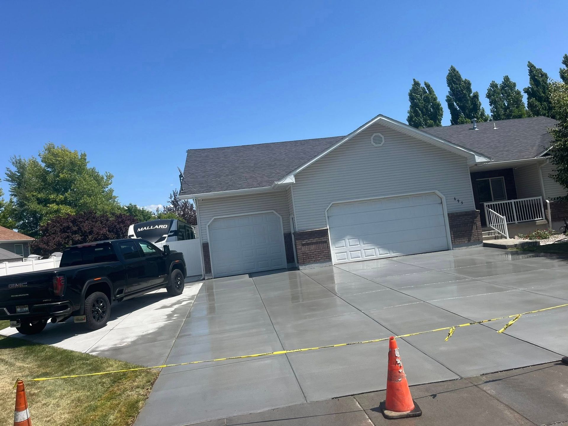A black pickup truck parked on a gravel area next to a newly poured concrete driveway at a single-story house.