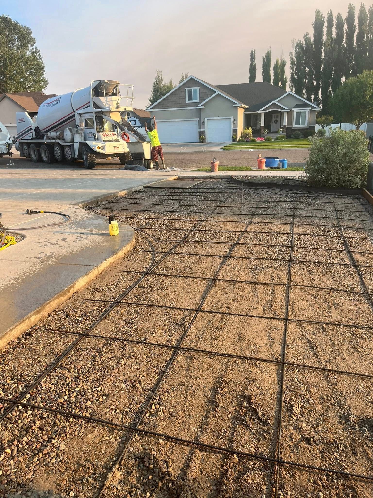A concrete truck prepares to pour cement over a gravel driveway prepped with a metal rebar grid in front of a house.