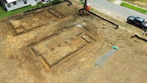 An aerial view of a construction site showing two rectangular foundation trenches dug into a cleared dirt lot.