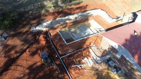 An aerial view of a backyard construction site showing a pool foundation, drainage pipes, and excavating equipment.