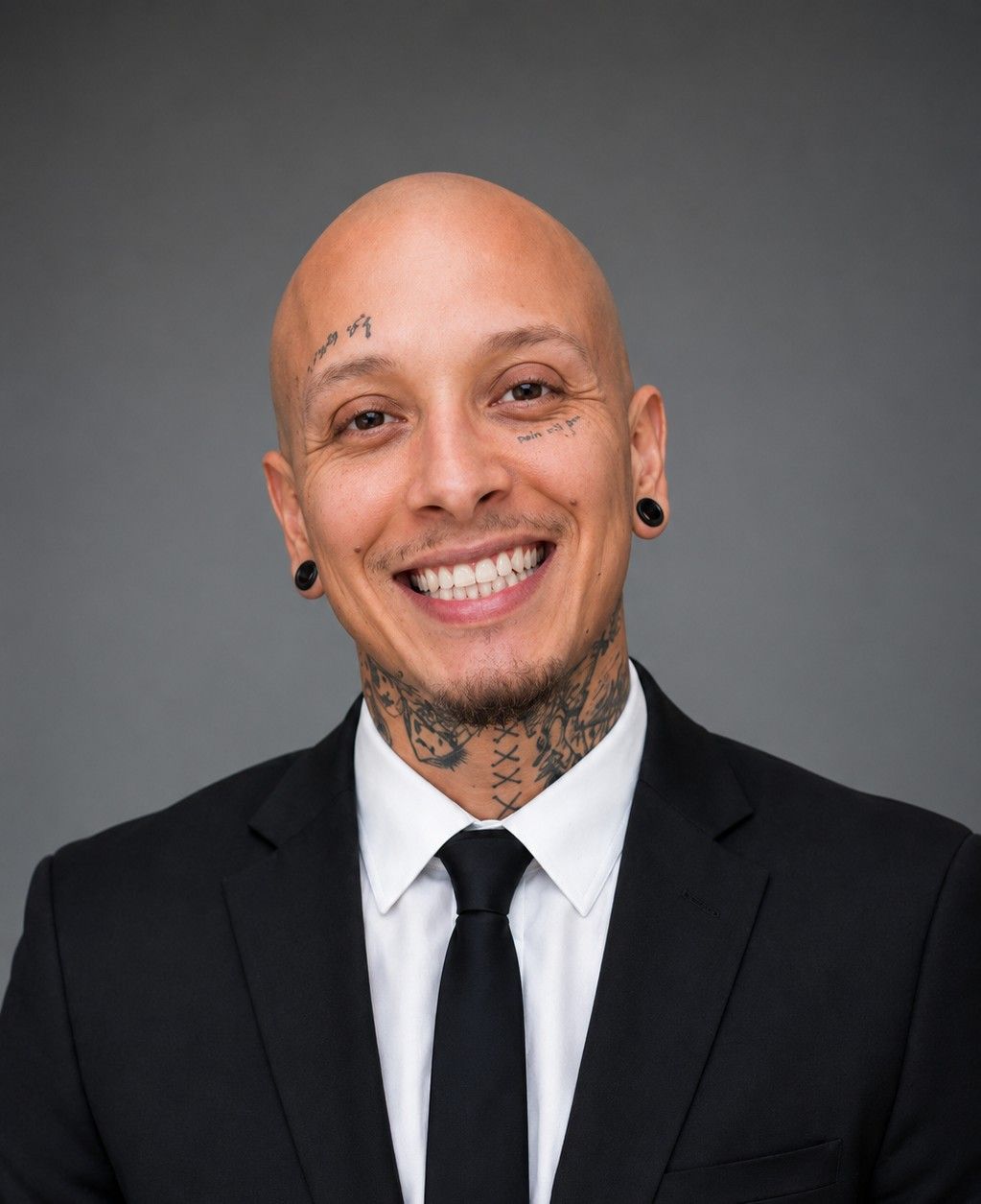 Smiling person in a black suit and tie against a gray background